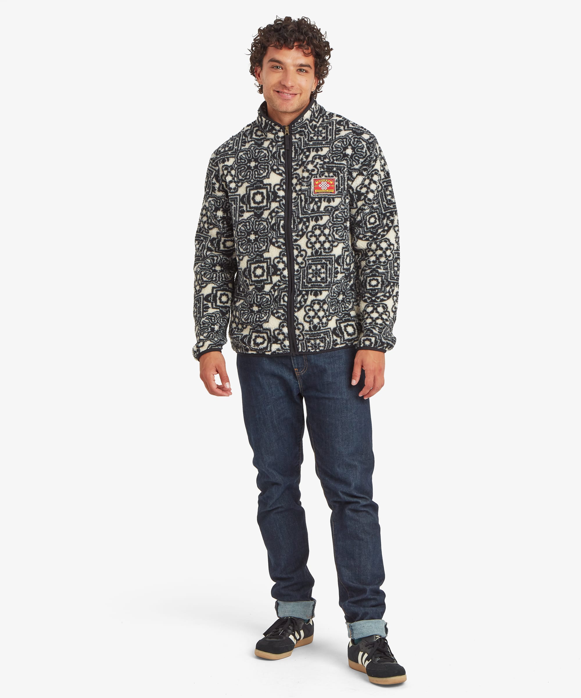 Full-body front view of a black printed full-zip fleece jacket featuring an allover geometric pattern. Styled with jeans and showcasing a stand collar and zip-front design.