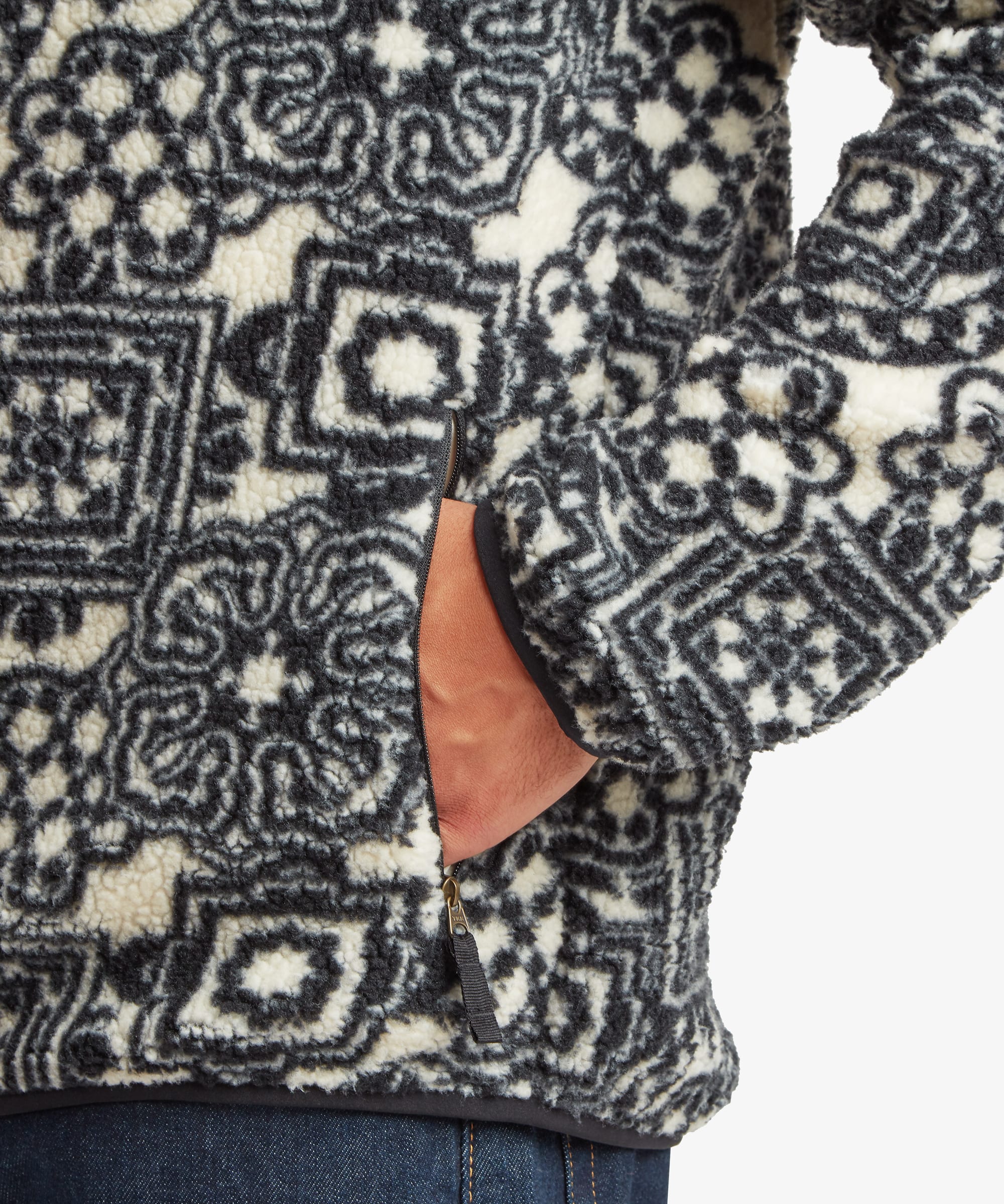 Close-up of a black printed full-zip fleece jacket featuring an allover geometric pattern and side pocket detail.