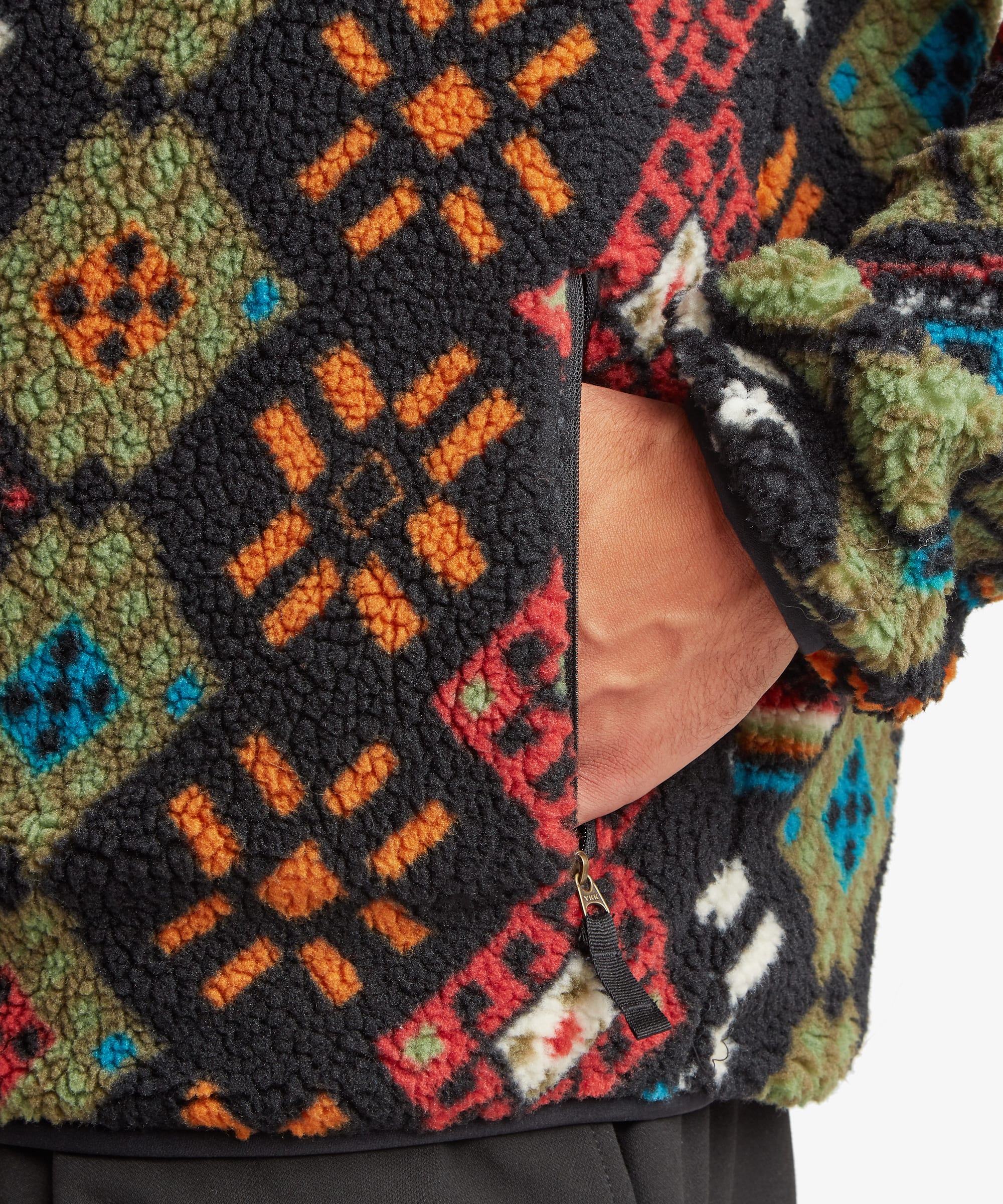 Close-up detail of the Sherpa Tarcho Printed Full Zip Jacket in black showing the colourful geometric fleece pattern, the side pocket opening and the soft textured fabric.