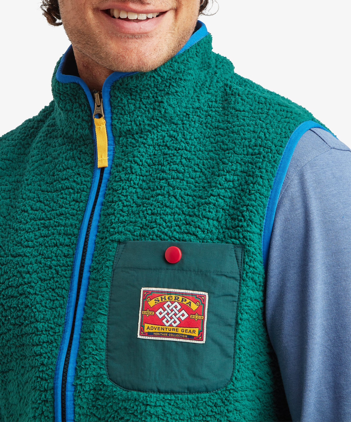 A close up of a man wearing a green fleece vest with contrasting blue binding on the zip and arms.
