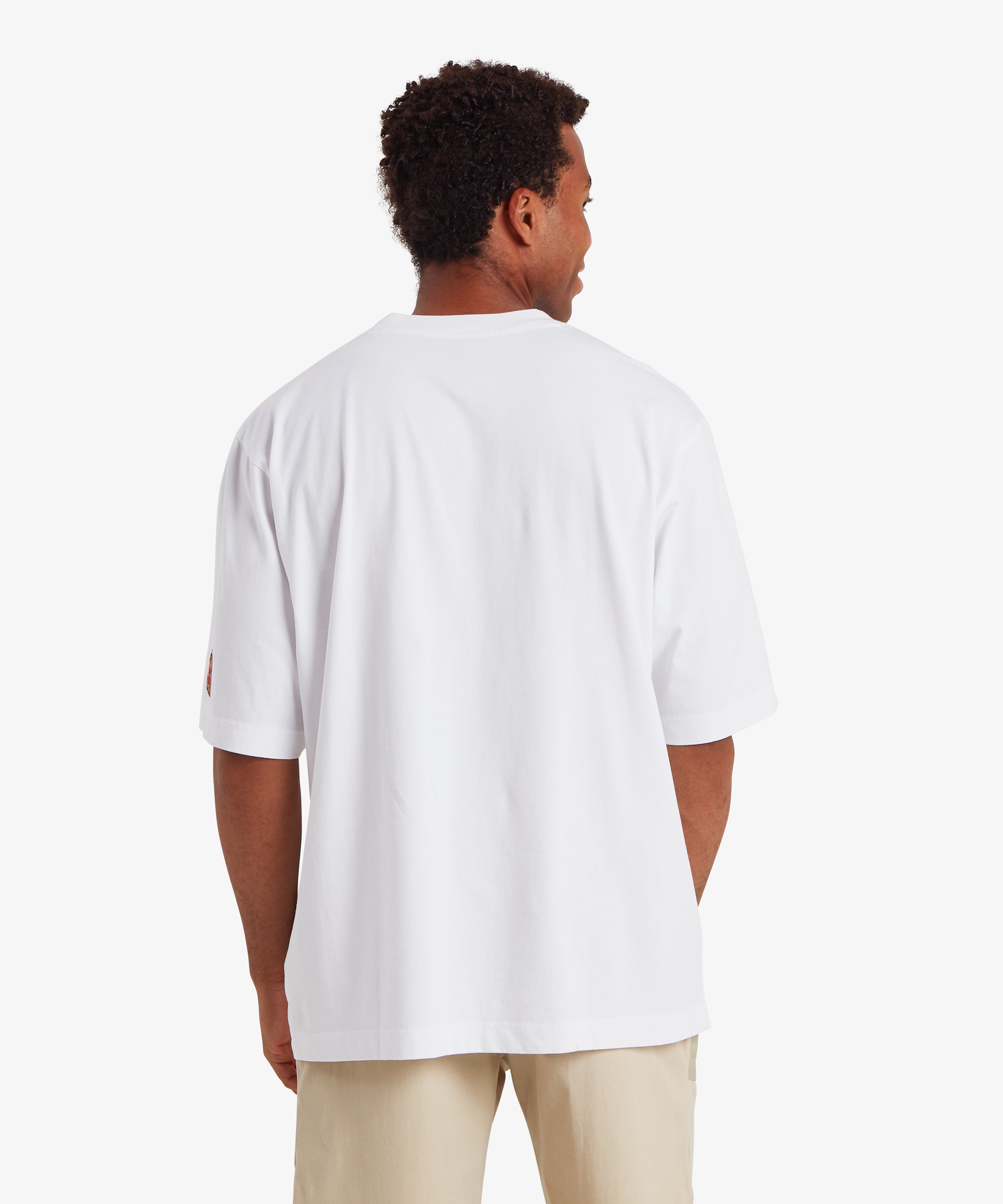 A back view of a man wearing relaxed fit white T-shirt. The T-shirt is plain of the man with no graphic or detail. The T-shirt is paired with beige shorts.