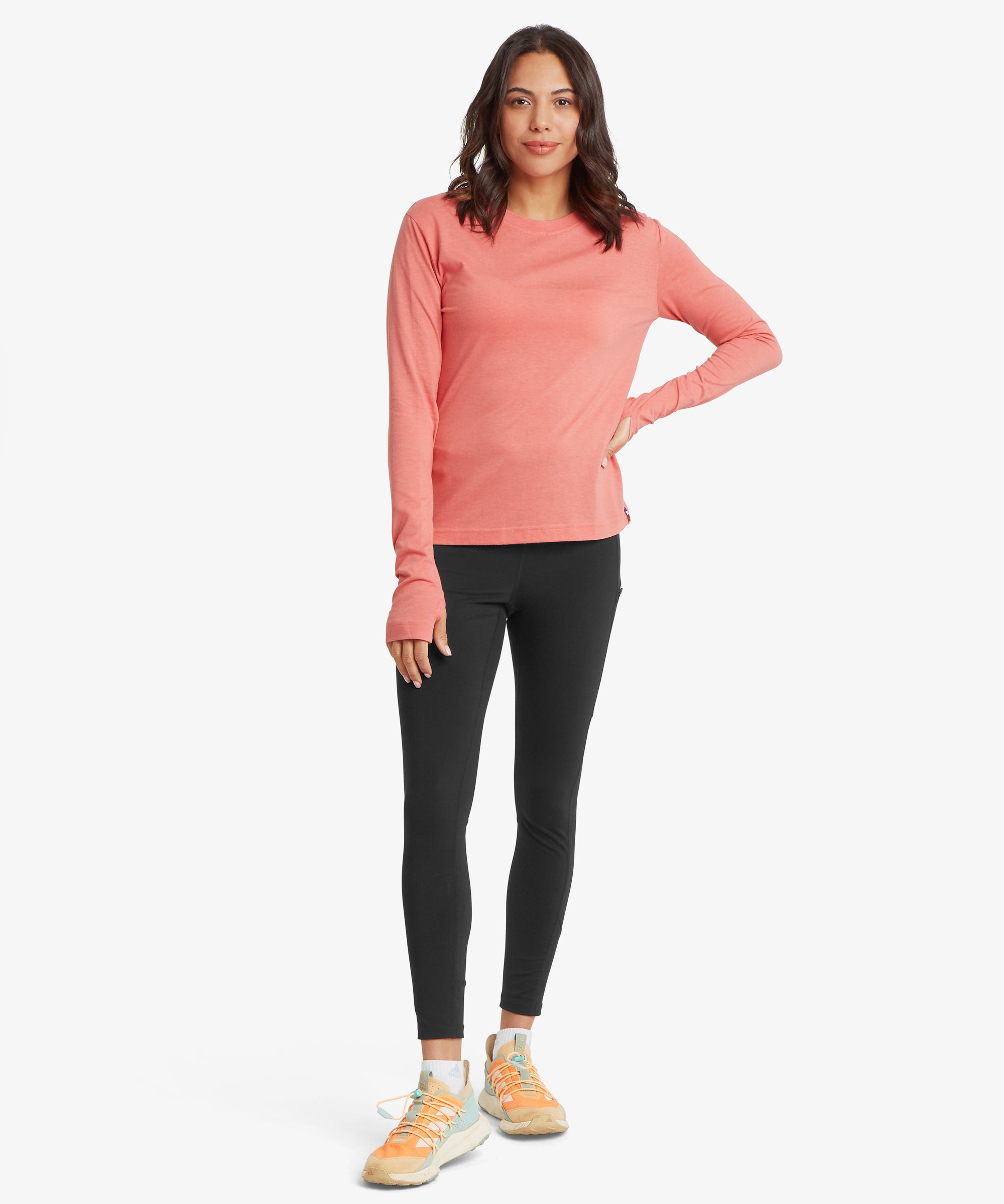 Woman wearing a coral long-sleeve top and black leggings on a white background