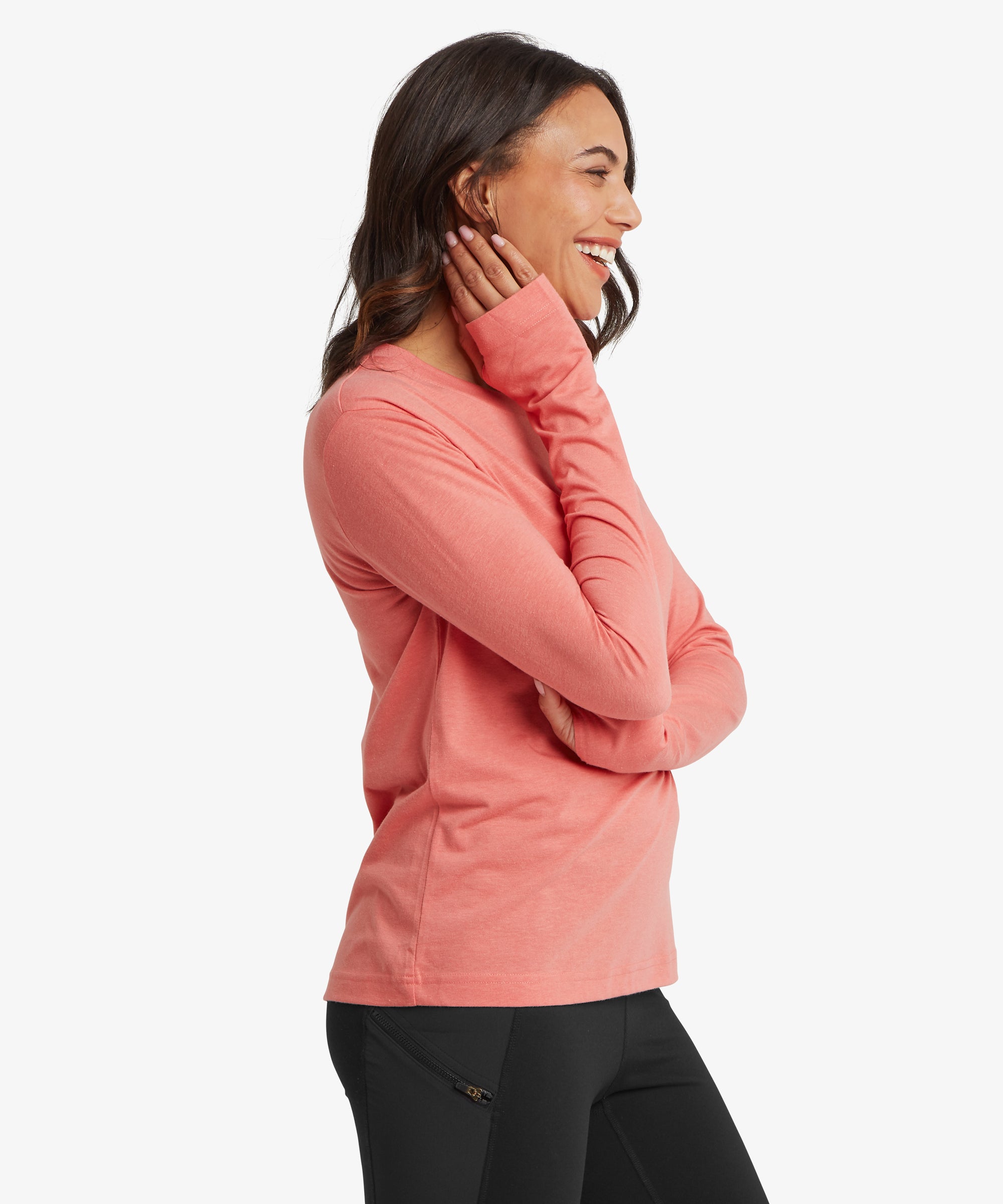 Side view of the Sherpa Bali Long‑Sleeve Tee in coral pink styled with black leggings, showing the lightweight knit, relaxed silhouette, and extended sleeves ideal for layering and active days.