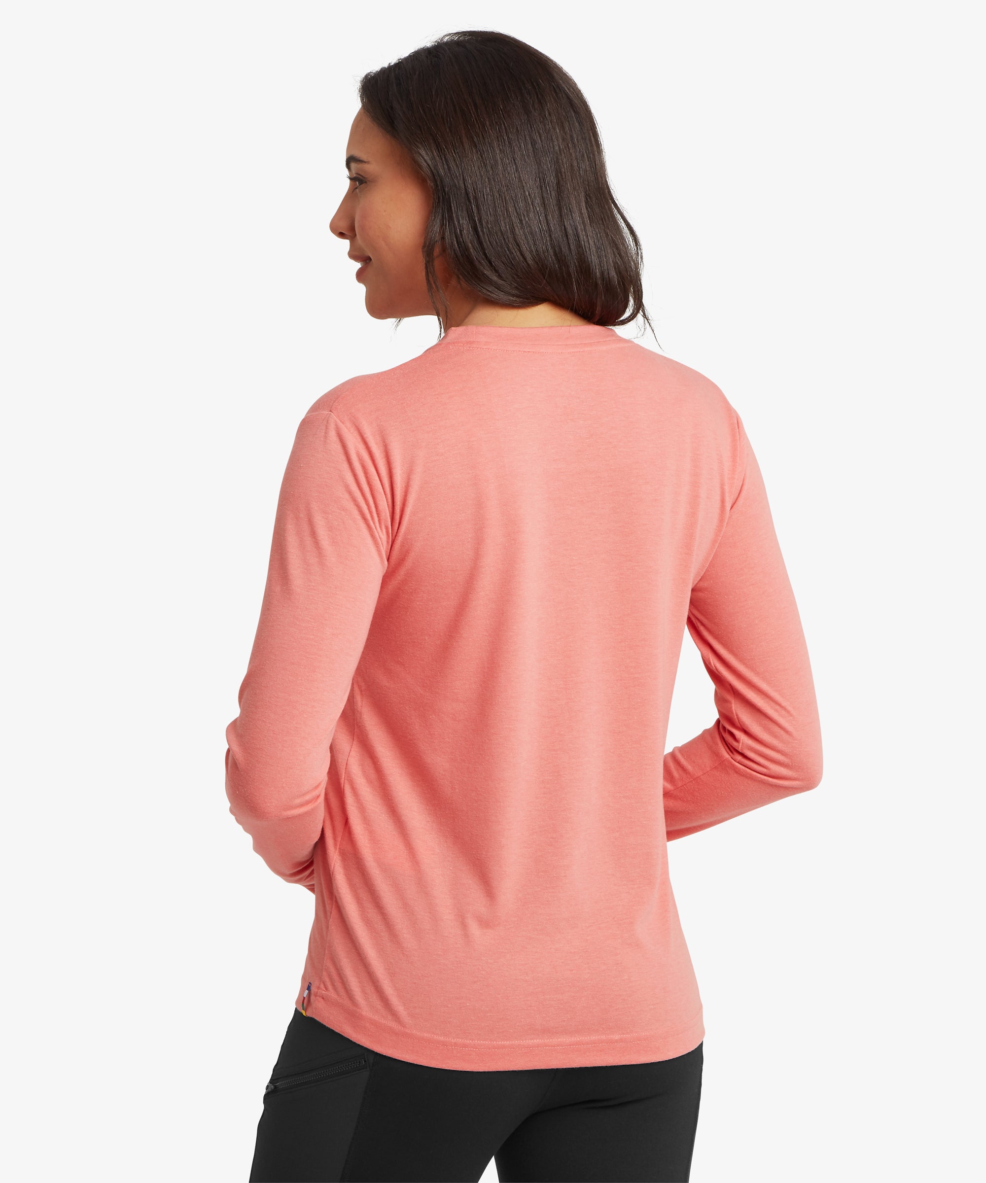 Rear view of the coral pink Sherpa Bali Long‑Sleeve Tee paired with black leggings, highlighting the smooth drape, straight back panel, and casual everyday fit designed for breathable comfort.