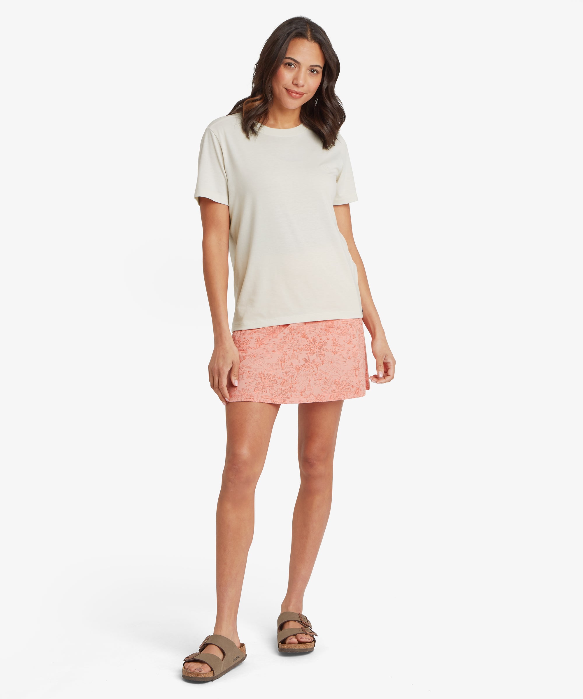 Front view of the off‑white Sherpa Bali Tee styled with a coral patterned skirt, featuring a clean crew neckline, soft breathable knit, and versatile everyday fit for warm‑weather styling.