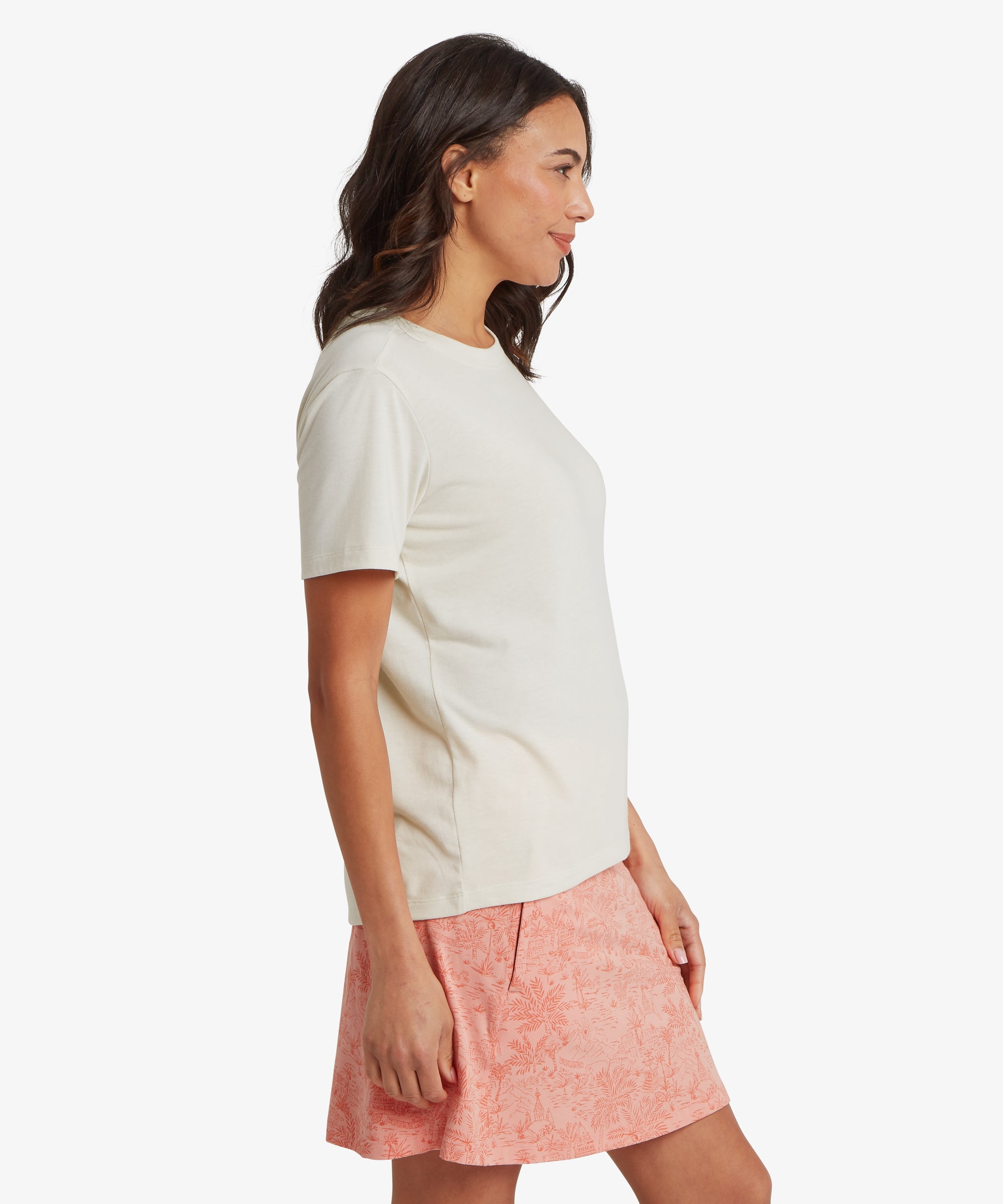 Side profile of the off‑white Sherpa Bali short‑sleeve T‑shirt styled with a coral patterned skirt, highlighting the relaxed silhouette, straight hem, and smooth cotton‑blend knit designed for all‑day comfort.