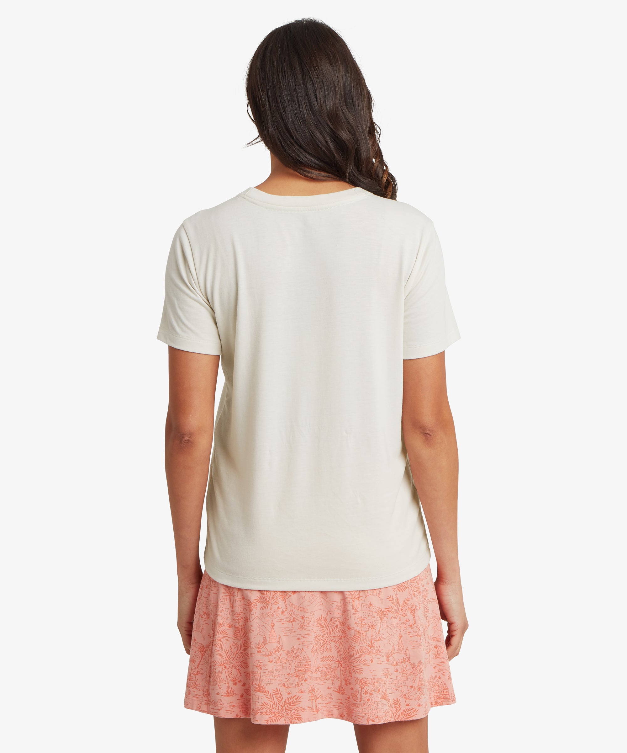 Rear view of the off‑white Sherpa Bali short‑sleeve tee paired with a coral patterned skirt, showing the soft drape, rounded crew neckline, and breathable jersey ideal for everyday wear.