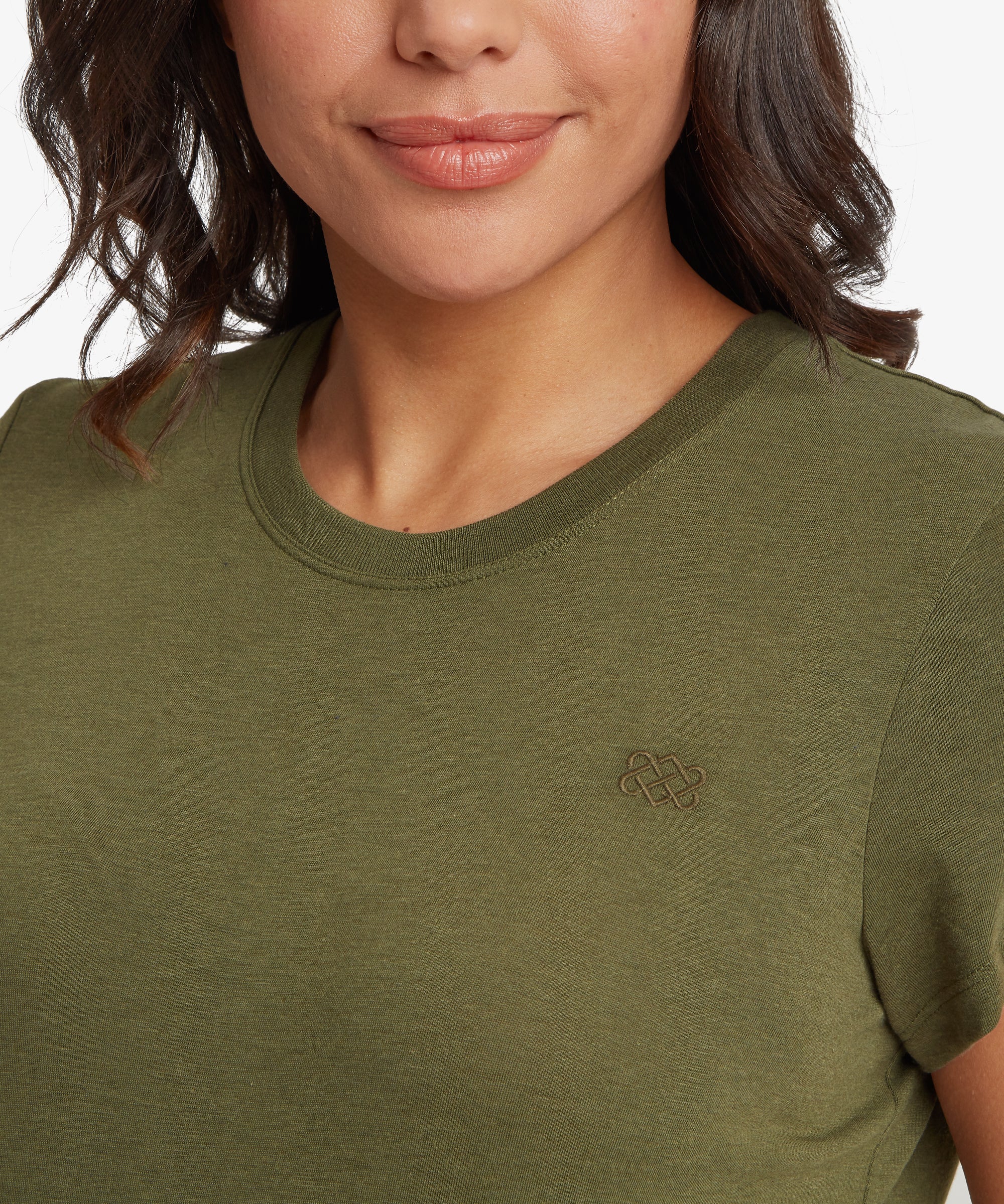 Close‑up view of an olive green women’s short‑sleeve crew‑neck T‑shirt, highlighting the fine knit texture and the small tonal embroidered endless‑knot logo on the left chest. The ribbed neckline and smooth lightweight fabric are clearly visible, showing the comfortable, relaxed fit across the upper torso.