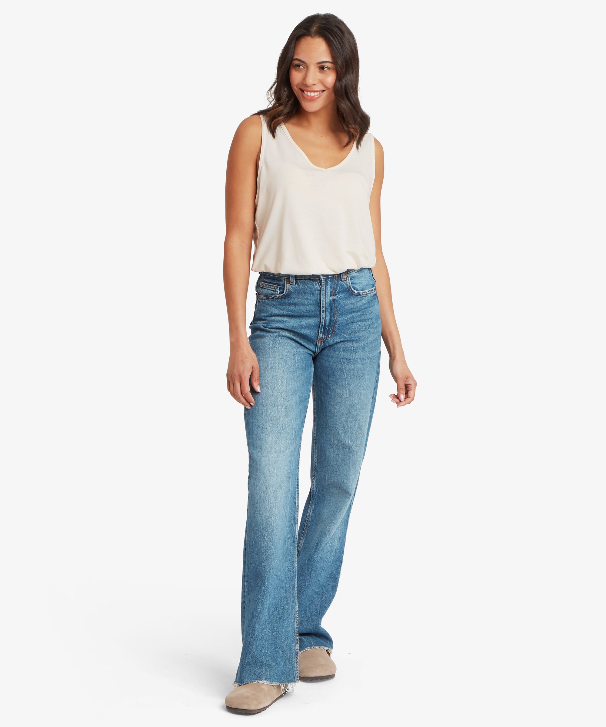 Full‑body front view of a cream women’s V‑neck tank top styled with mid‑wash denim jeans. The tank’s lightweight material and relaxed fit are visible as the wearer walks forward, showcasing the casual everyday silhouette.