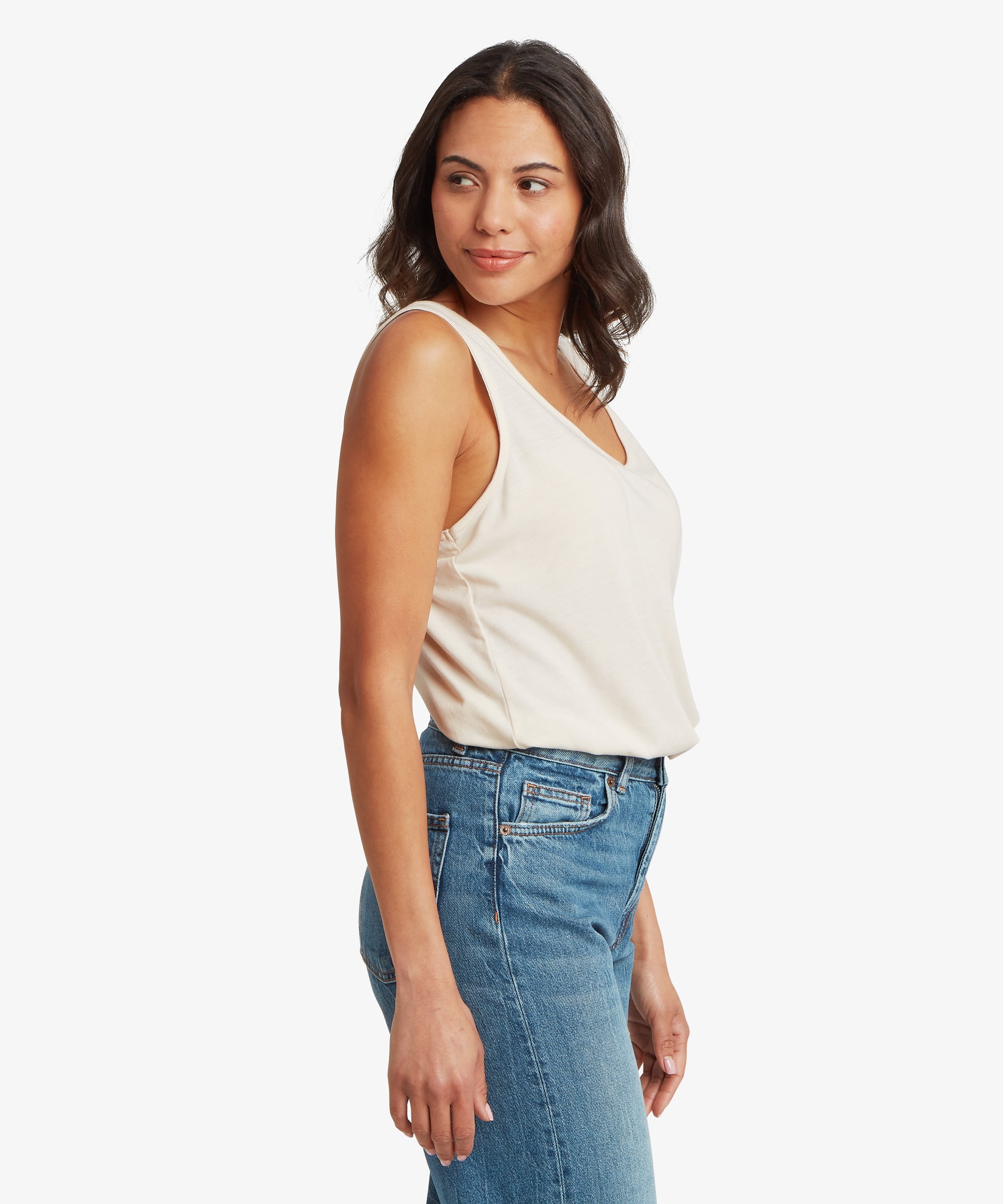 Side view of a cream women’s V‑neck tank top paired with mid‑wash denim jeans. The tank features wide shoulder straps, a soft lightweight fabric, and a relaxed drape that sits comfortably at the hip
