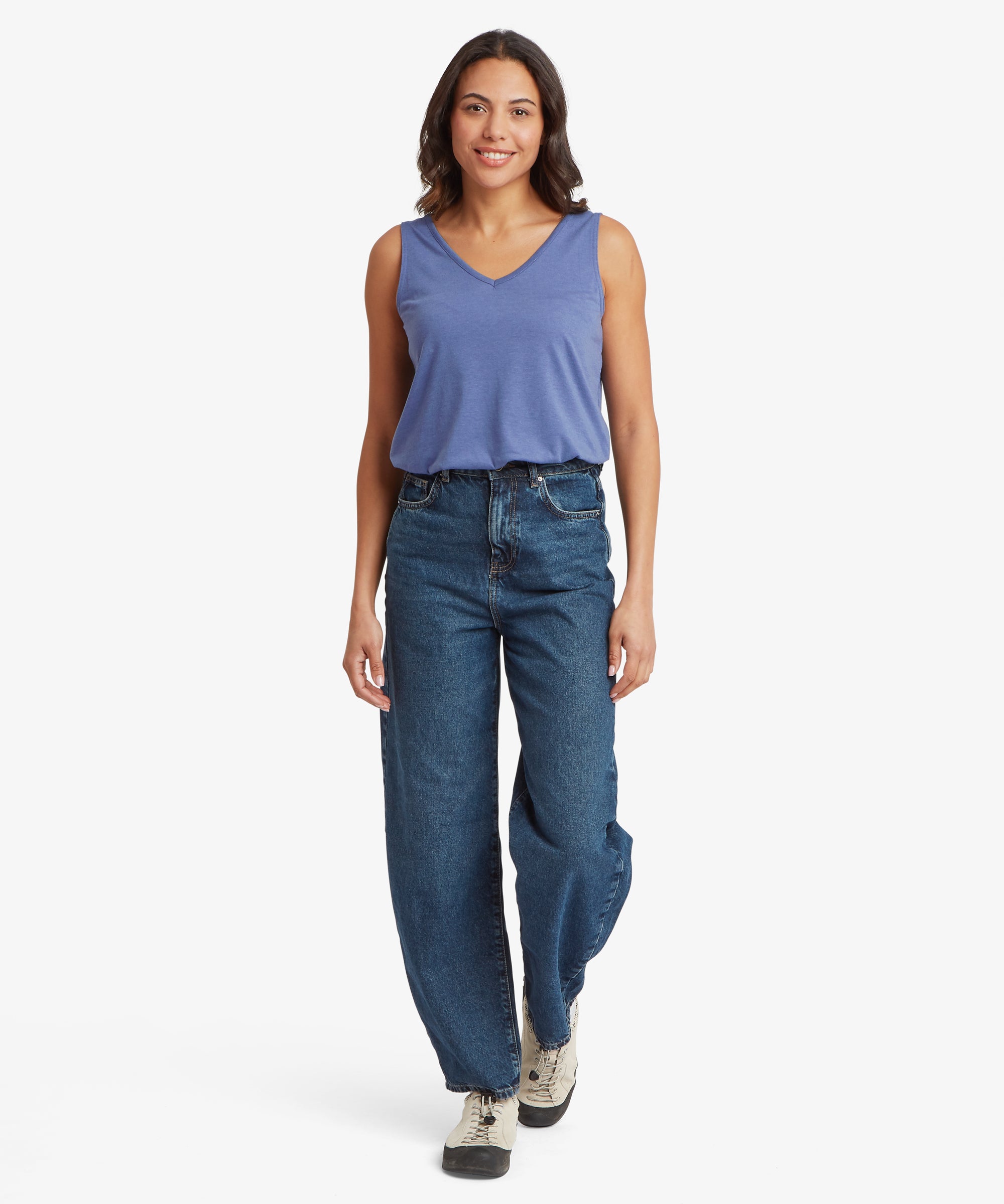 Full‑body view of a slate‑blue sleeveless V‑neck top paired with high‑waisted dark blue denim jeans, showing the relaxed drape of the lightweight jersey fabric and the easy, casual fit. The top is tucked loosely at the front, and the straight‑leg jeans are styled with light hiking shoes, creating a practical warm‑weather outfit suitable for travel, walking, and everyday wear