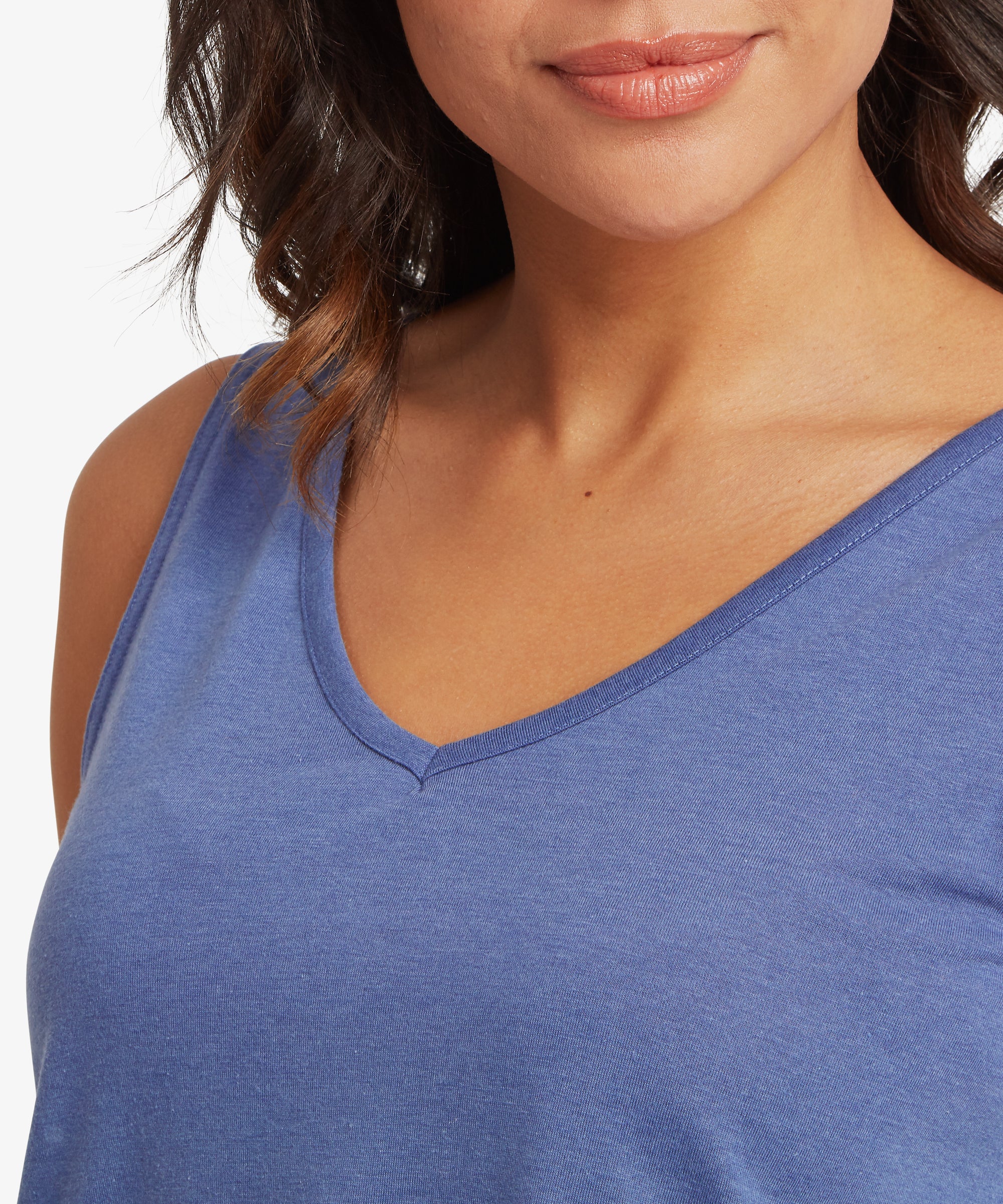 Close-up view of a sleeveless V‑neck top in a soft slate‑blue jersey fabric, showing the smooth texture, neat neckline stitching, and relaxed drape across the upper chest and shoulders. Subtle waves in the hair frame the top, highlighting the lightweight, breathable material ideal for warm‑weather layering and everyday comfort.