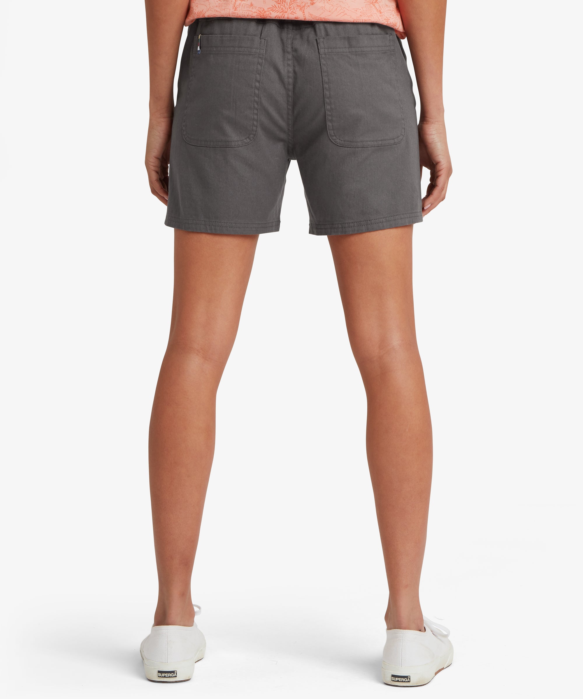 Back view of charcoal grey casual shorts paired with white canvas trainers and a coral patterned top. The shorts feature two large rear patch pockets, reinforced stitching, and a straight hem that sits mid‑thigh. The relaxed fit and durable woven fabric highlight a practical warm‑weather outfit suitable for walking, travel, and everyday outdoor activities.