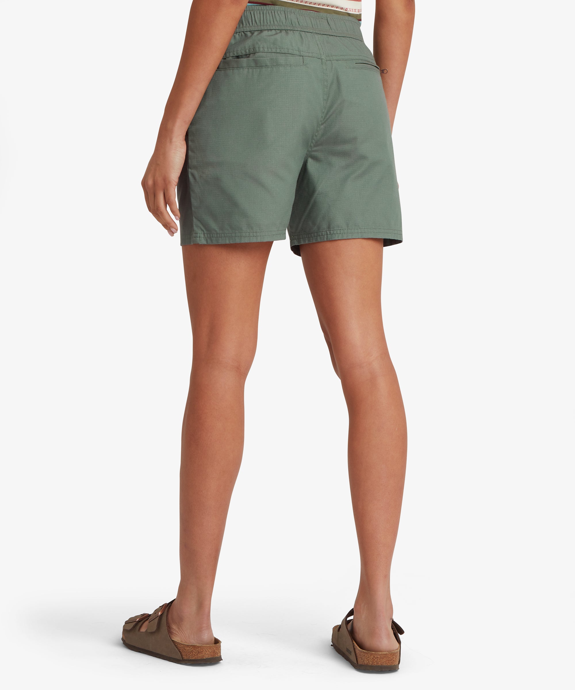 Three‑quarter front view of a sage green skort featuring large patch pockets, an elastic waistband with drawcord, and lightweight woven fabric. Paired with a patterned sleeveless top and sandals, the look highlights a casual, functional warm‑weather outfit ideal for sightseeing and outdoor activities