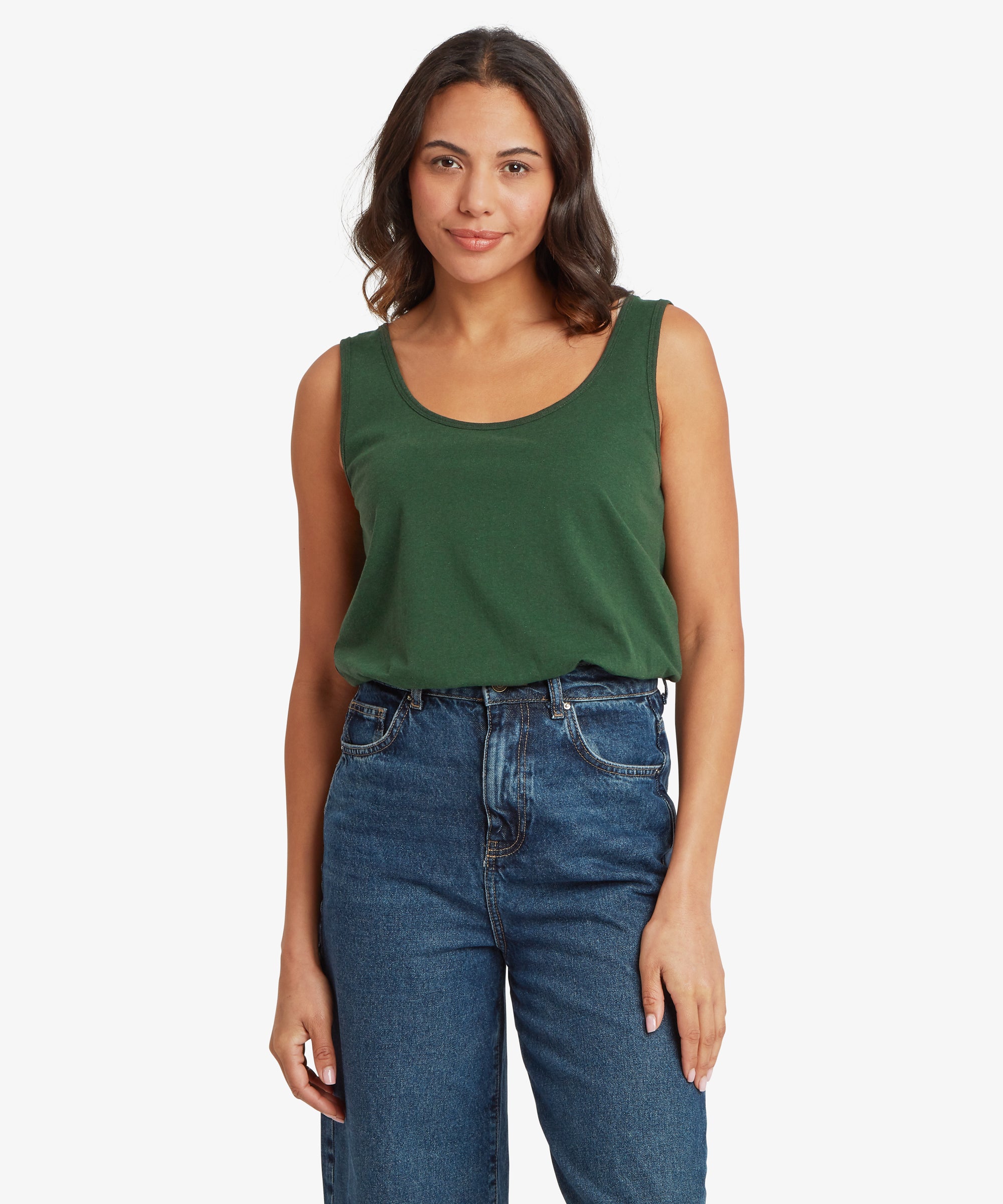Front view of a dark green scoop‑neck sleeveless top paired with high‑waisted blue denim jeans. The top has a relaxed drape and sits loosely at the waistband, showing the soft knit texture and simple, minimal design. Both arms rest naturally by the sides, and the jeans feature a classic straight‑leg cut with visible seam detailing.