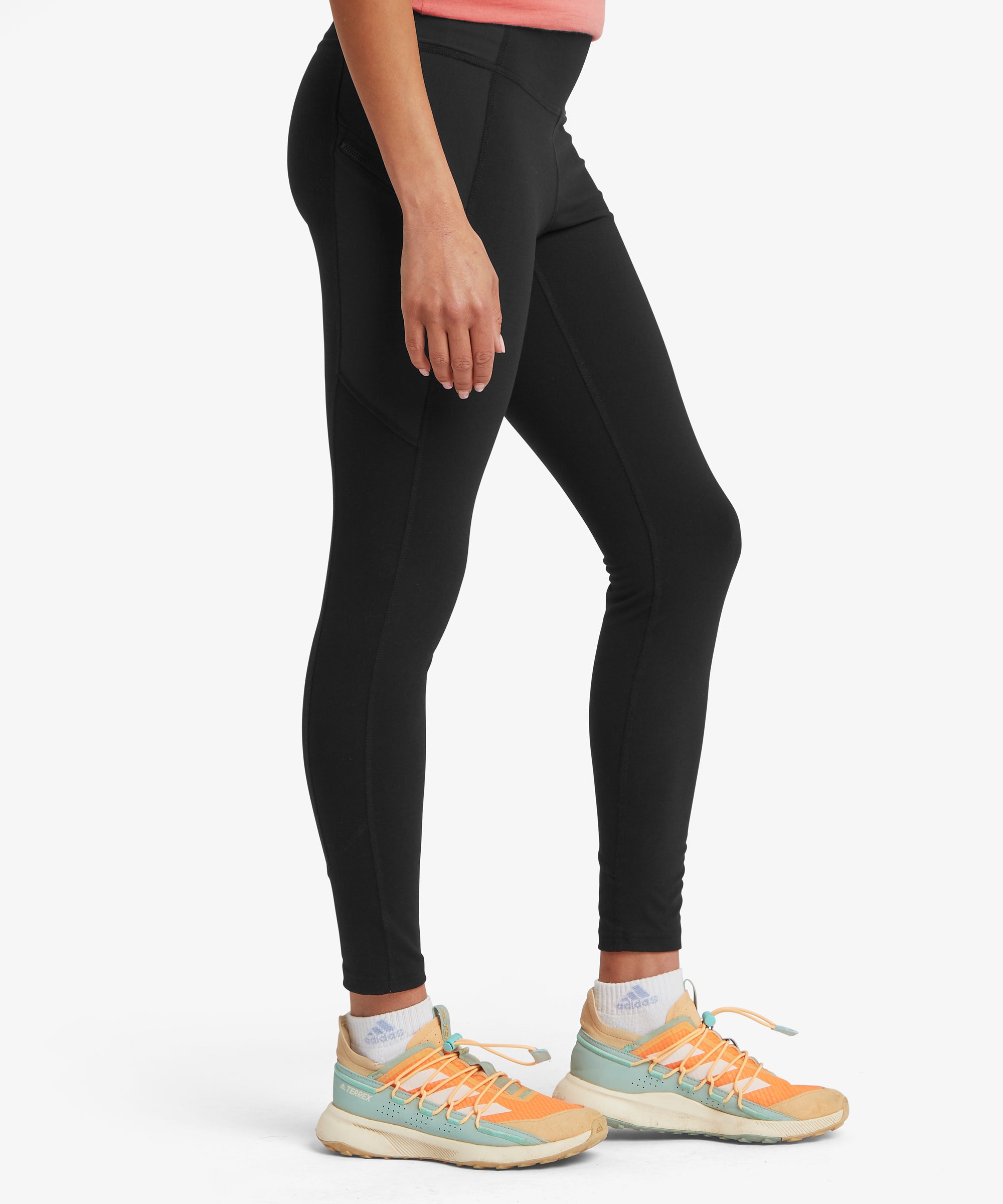 Side view of black full‑length leggings paired with light-colored athletic shoes featuring orange and teal accents.