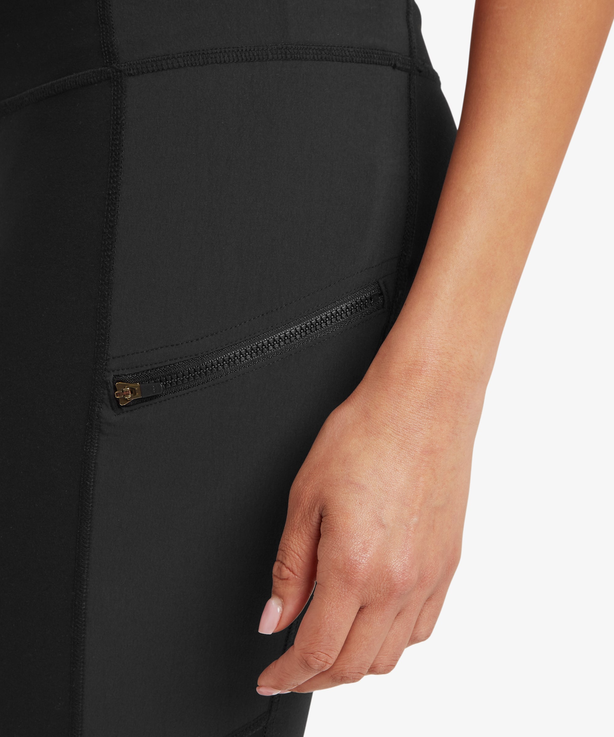 Close-up of a person wearing black leggings, showcasing the zip with a hand touching the fabric.