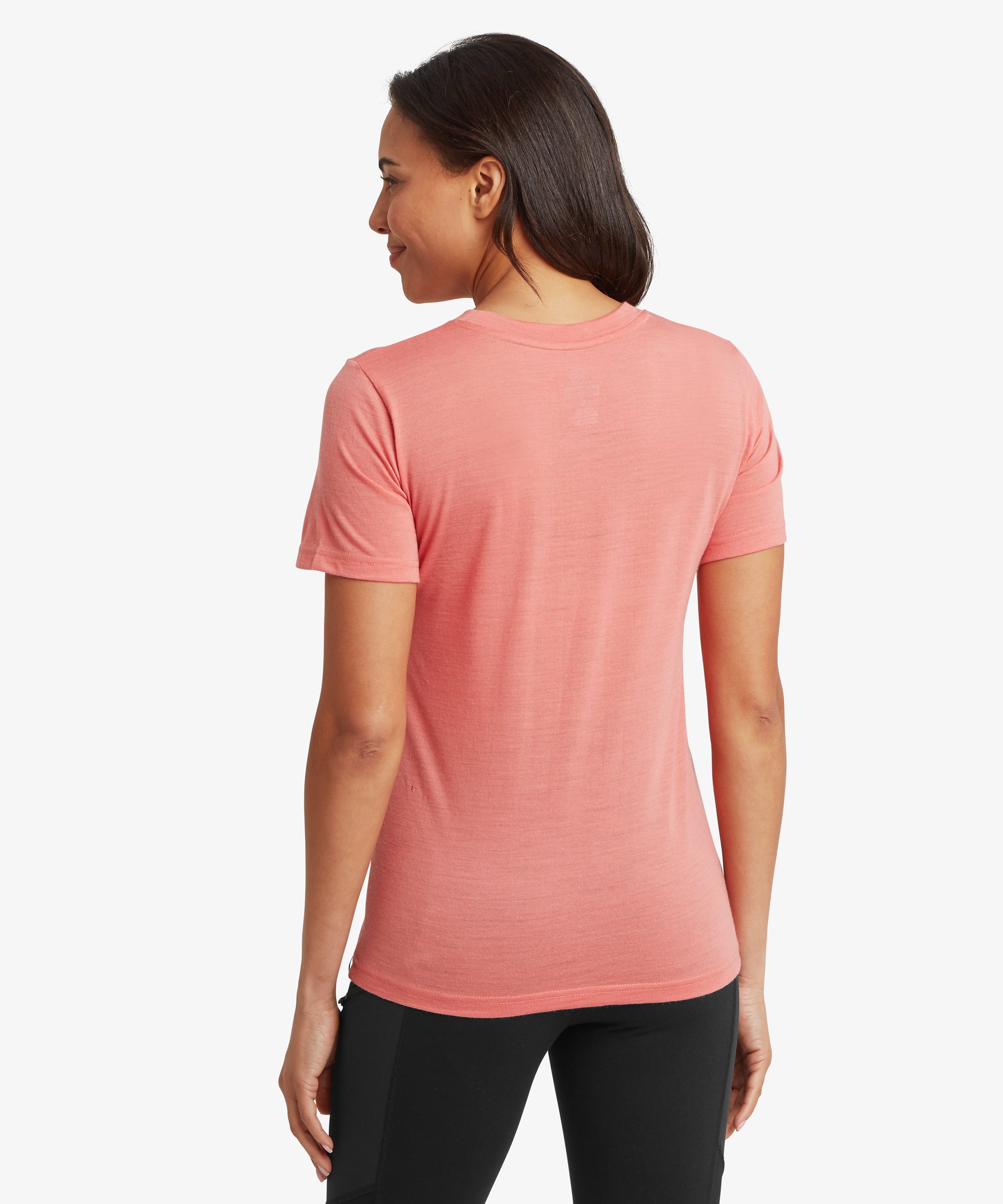 A back view of a person wearing a plain coral short‑sleeve T‑shirt and black trousers. Their straight dark hair falls to the upper back, and the white background highlights the garment’s simple design.