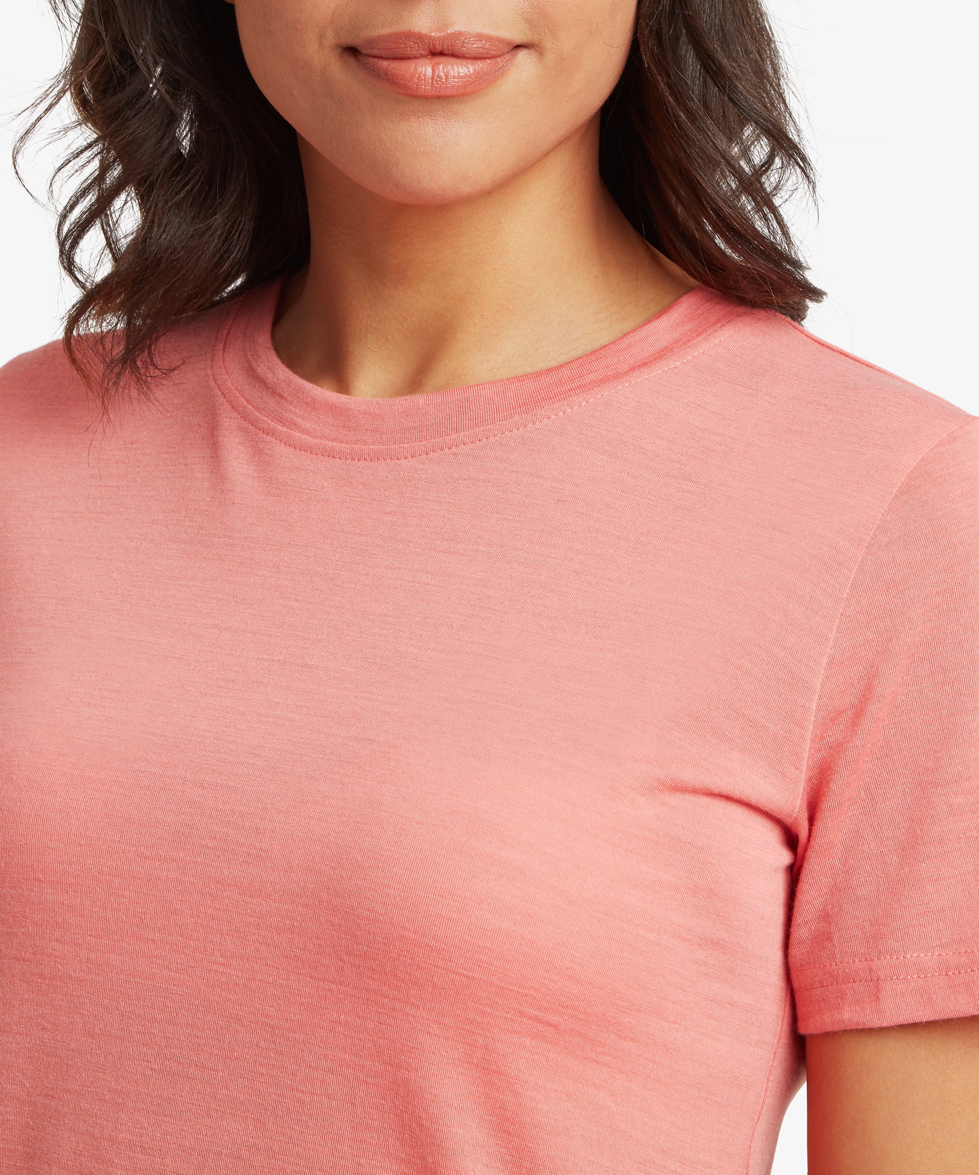 A close-up of a person wearing a plain coral short‑sleeve crew‑neck T‑shirt. The smooth fabric and relaxed fit are clearly visible, with dark shoulder‑length hair framing the neckline.