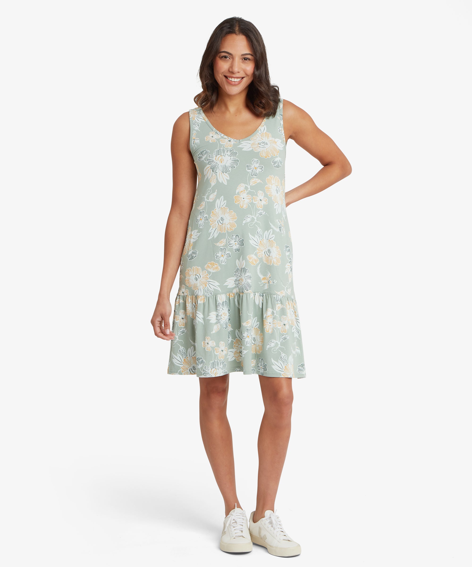 Vorderansicht eines grŸnen, Šrmellosen Blumenkleids mit gerŸschtem Saum, kombiniert mit wei§en Sneakers.