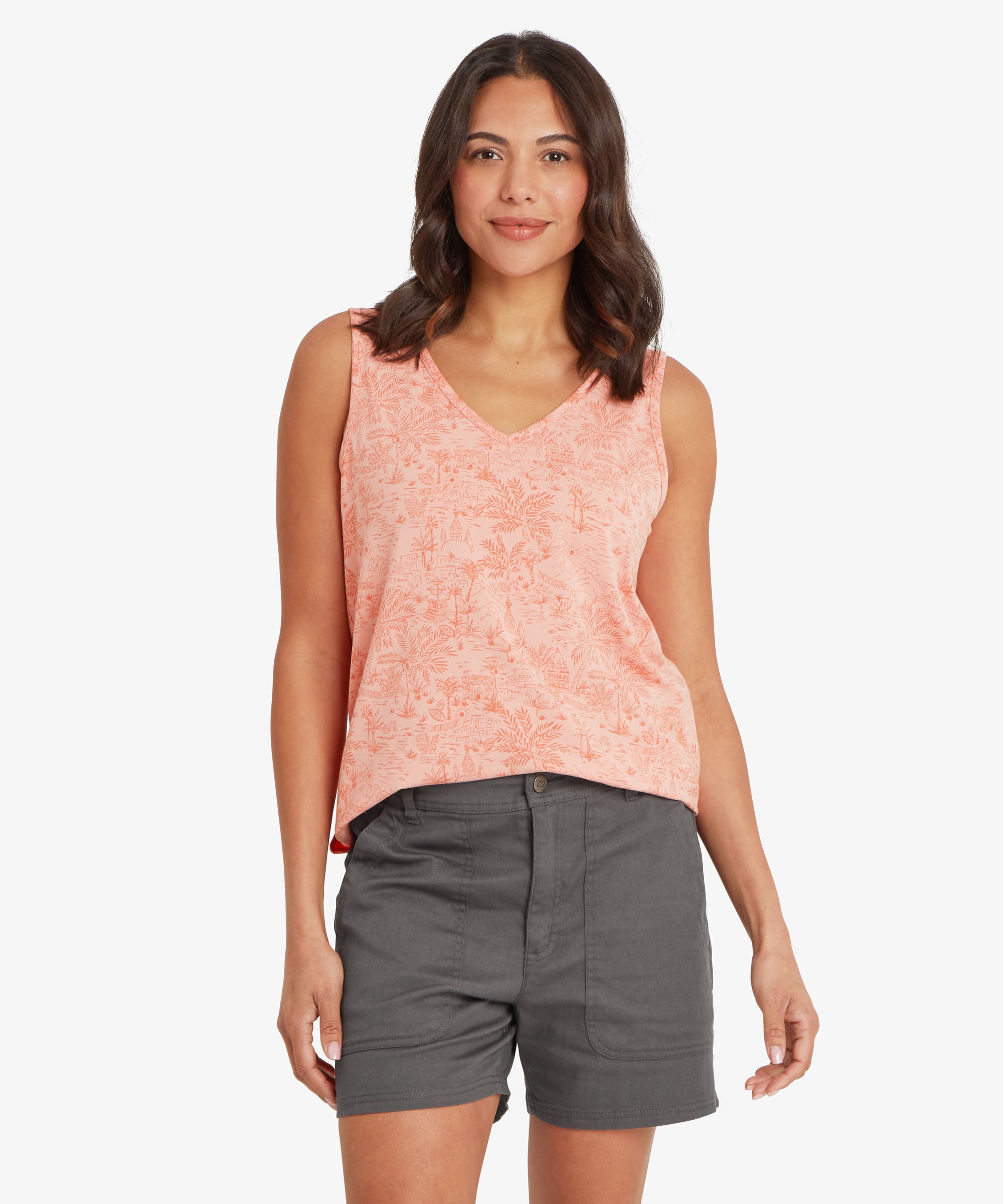 Woman standing facing forward wearing a peach sleeveless V-neck top with a relaxed fit through the torso, paired with dark grey shorts; her arms rest naturally at her sides and she has a calm, neutral expression.