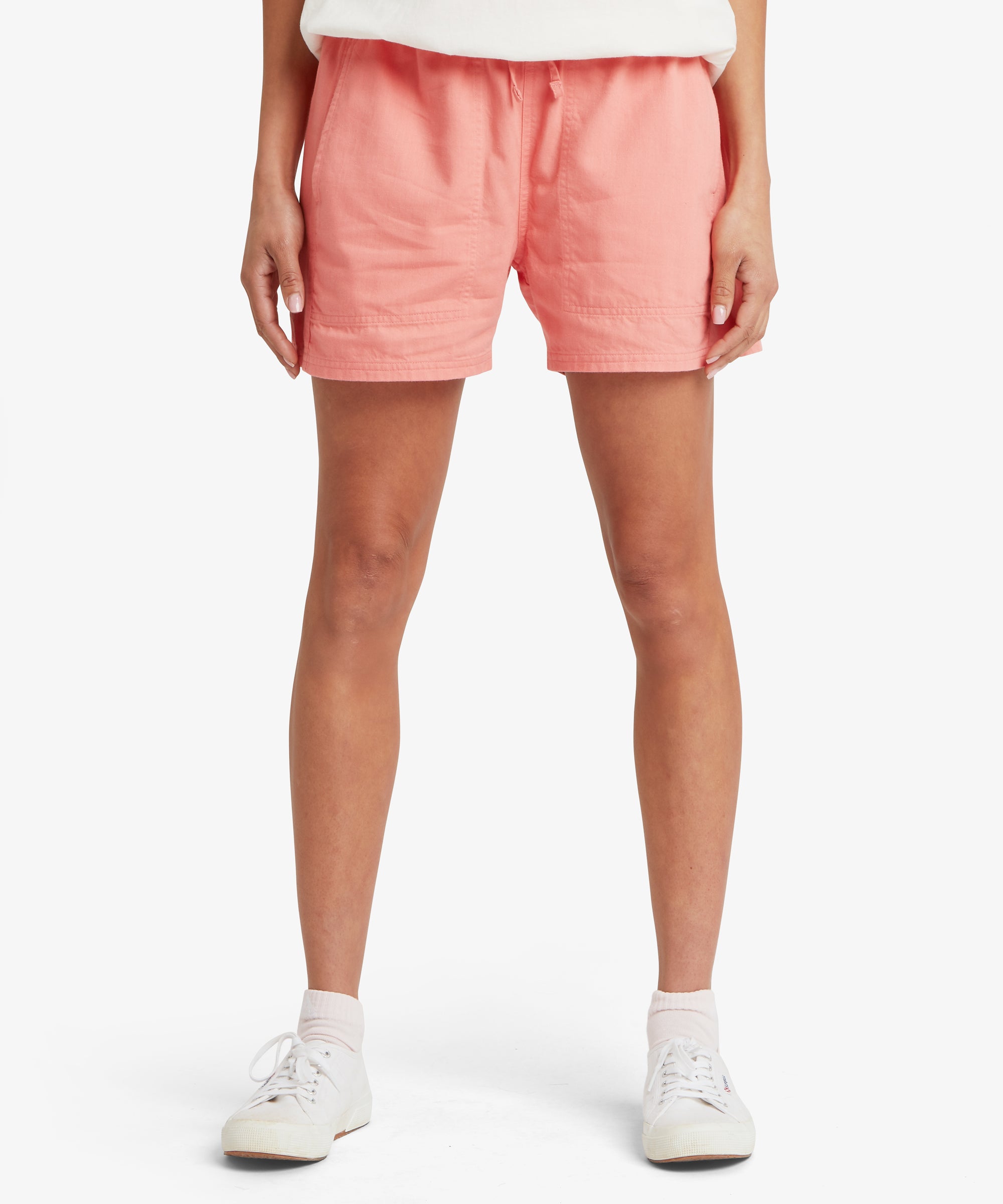 Front view from waist to knees of a woman wearing coral-pink shorts with a relaxed fit, elastic waistband, and mid-thigh length.