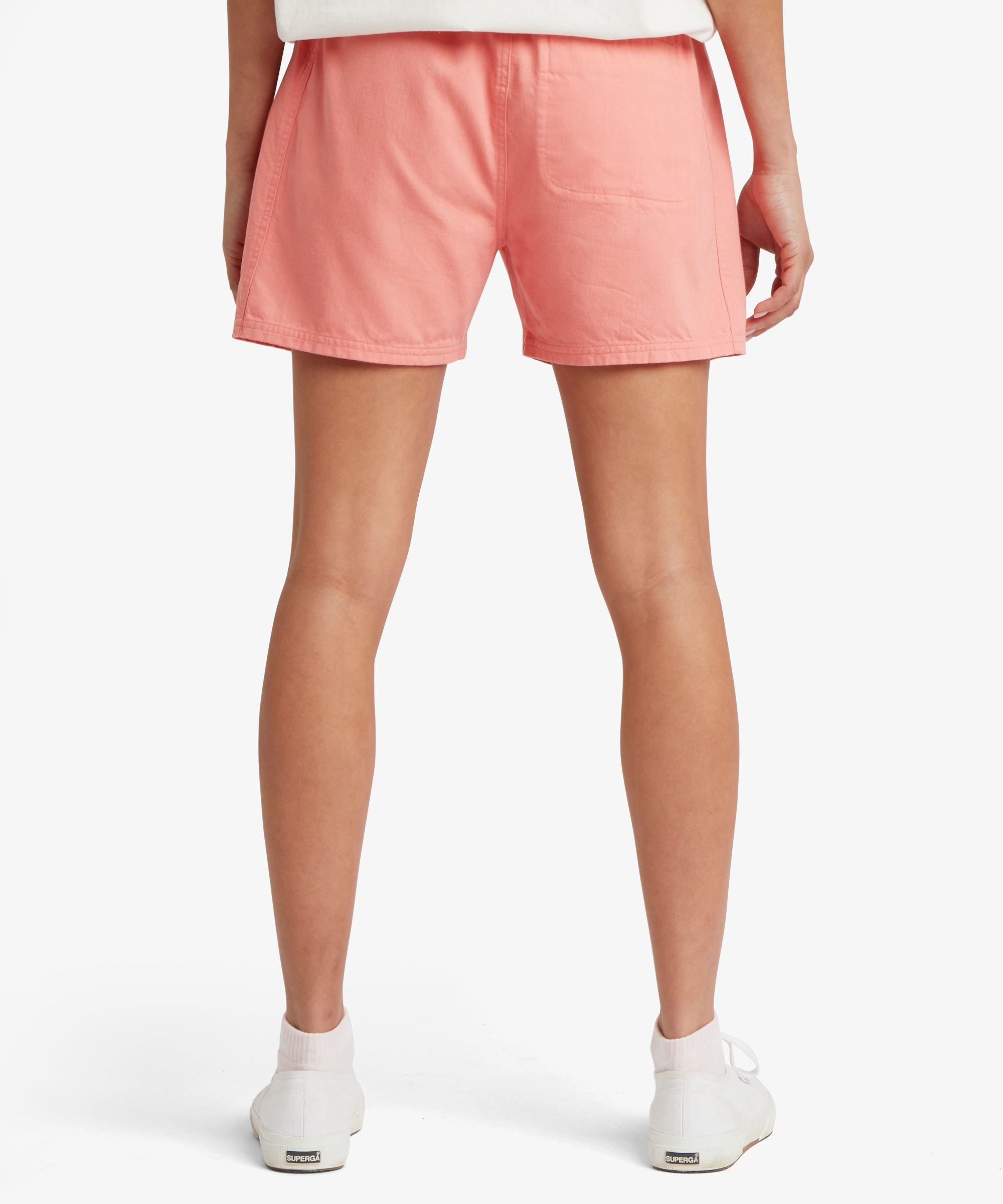 Back view of a woman wearing coral-pink shorts with an elastic waistband, relaxed fit, and straight hem at mid-thigh.