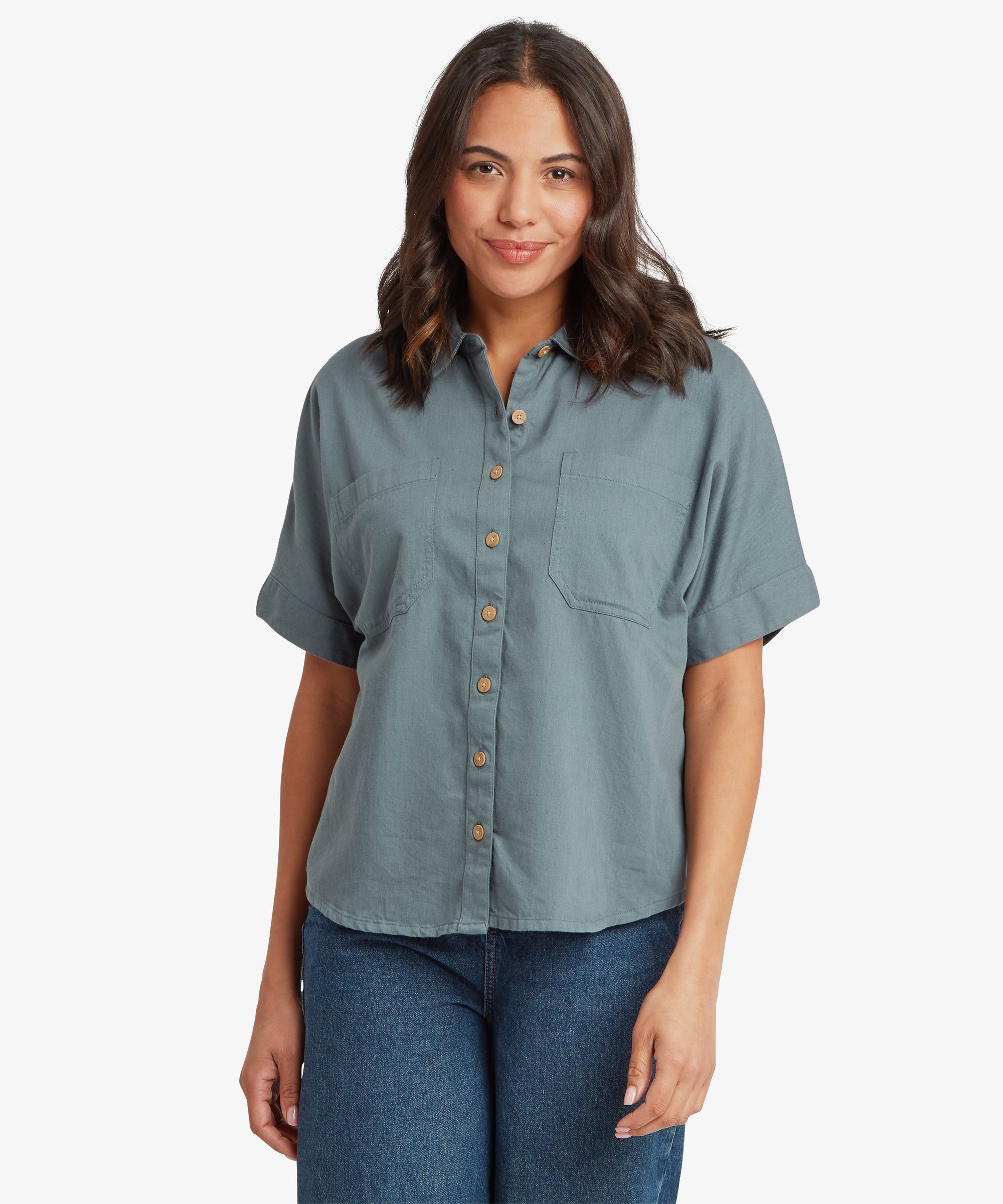 Woman wearing a blue-grey short-sleeve button-up shirt with a relaxed fit through the body and sleeves, styled untucked with straight-leg jeans.