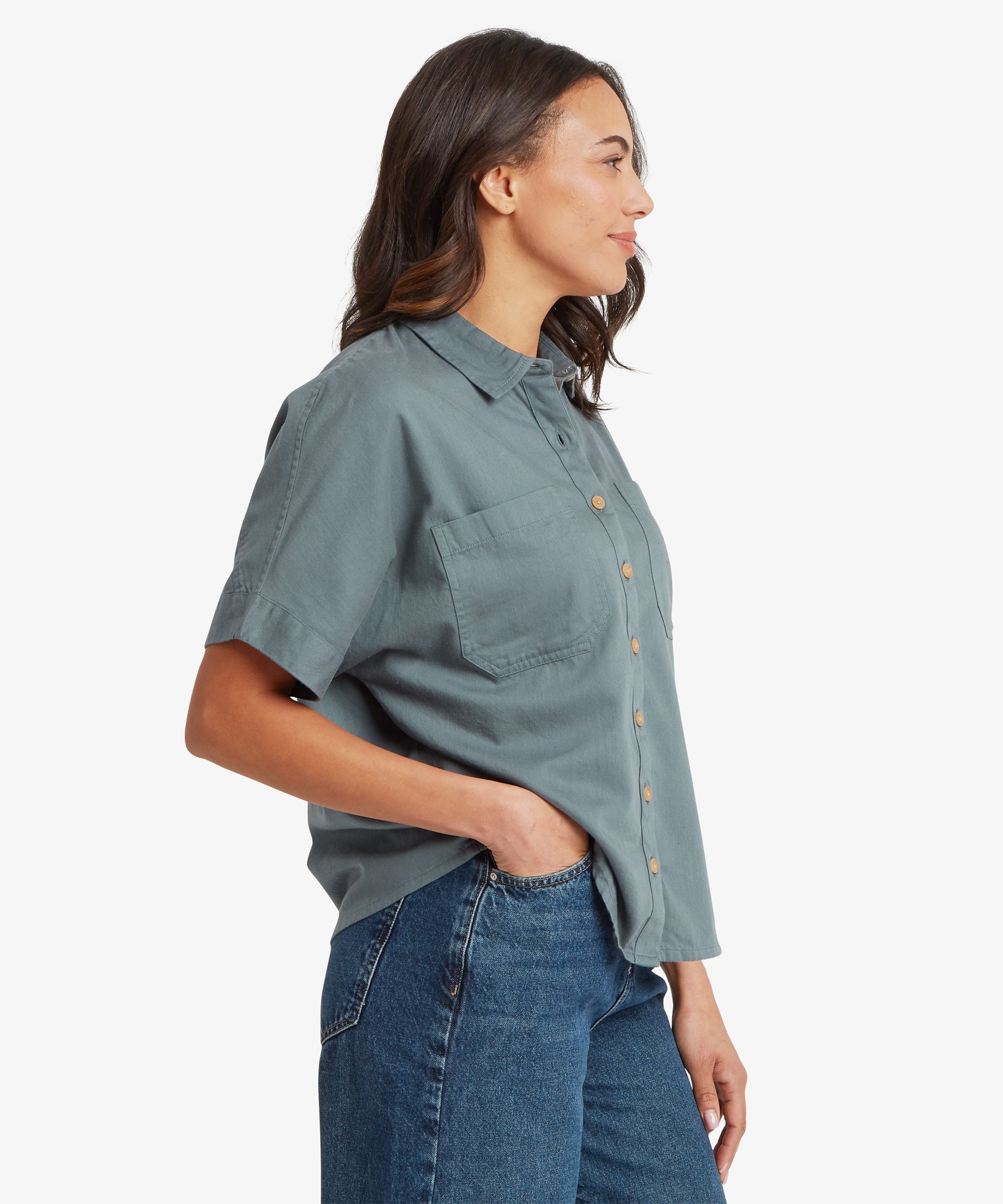 Side view of a woman wearing a blue-grey short-sleeve button-up shirt, showing the boxy fit through the torso and slightly dropped shoulder seam.