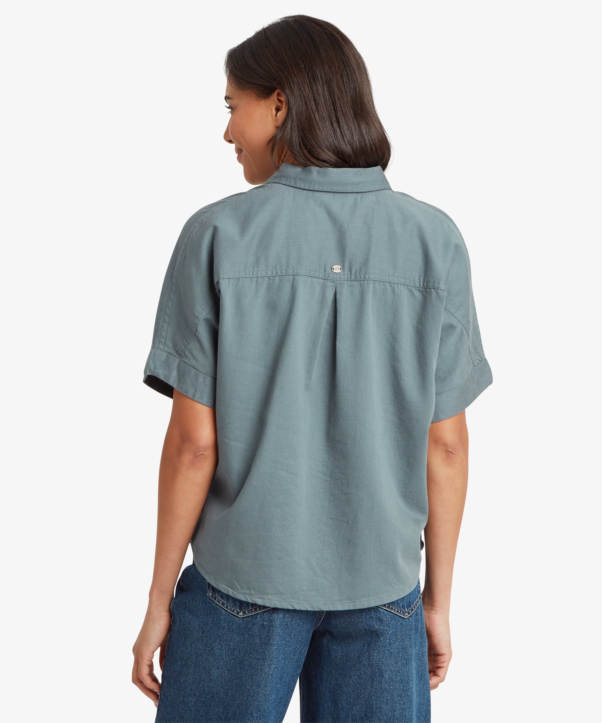 Back view of a woman wearing a blue-grey short-sleeve shirt with a straight hem and relaxed fit across the shoulders and upper back.