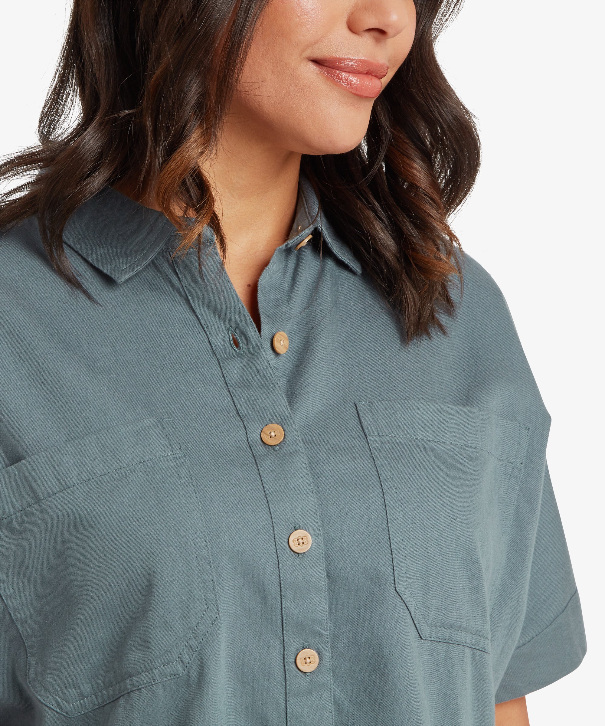 Close-up of the blue-grey shirt showing the pointed collar, chest pocket, and light wood-look buttons on a smooth woven fabric.