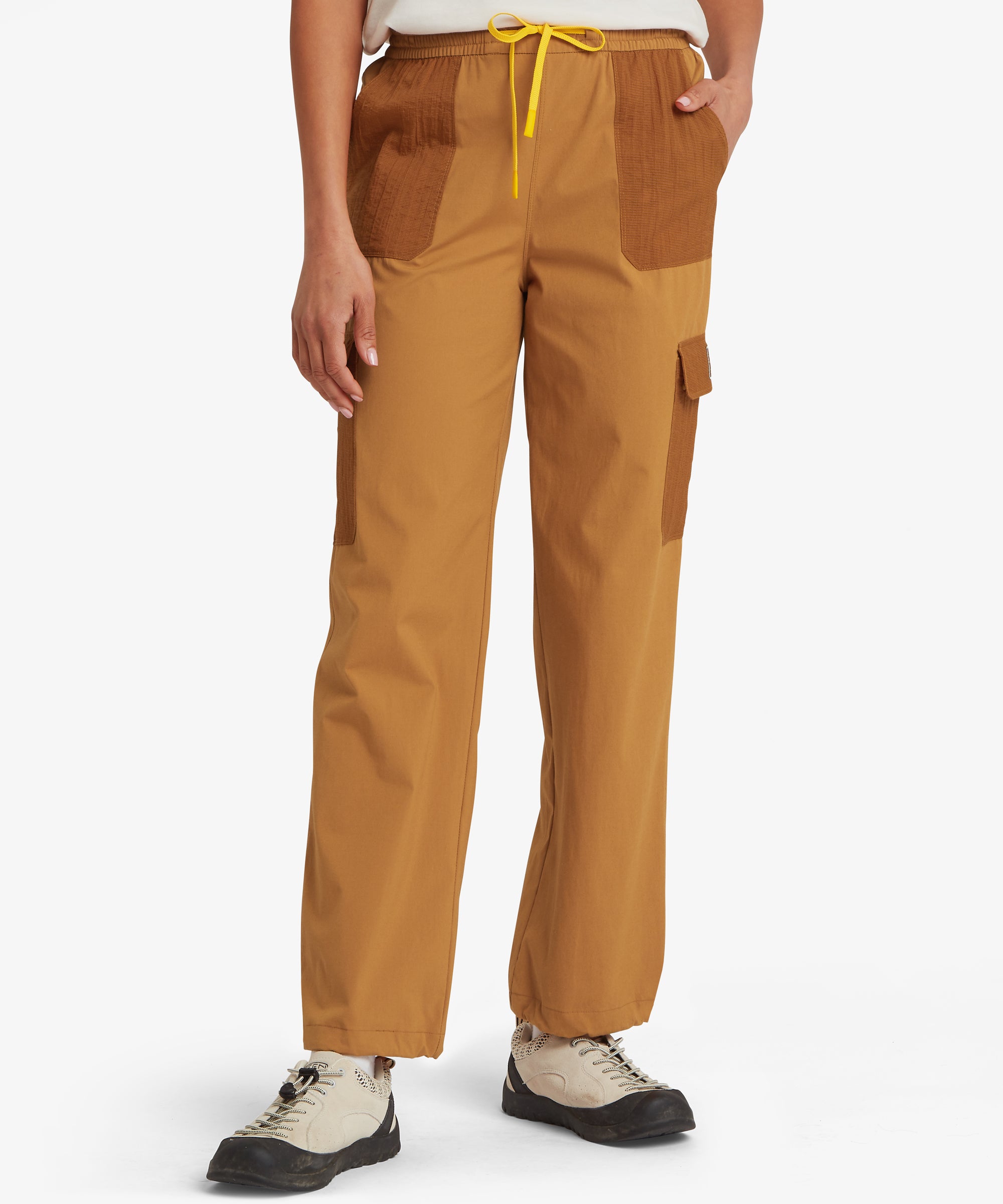 Front, lower body view of a woman wearing mustard-yellow straight-leg trousers, showing the relaxed fit through the hip and thigh and cropped ankle length with trainers.