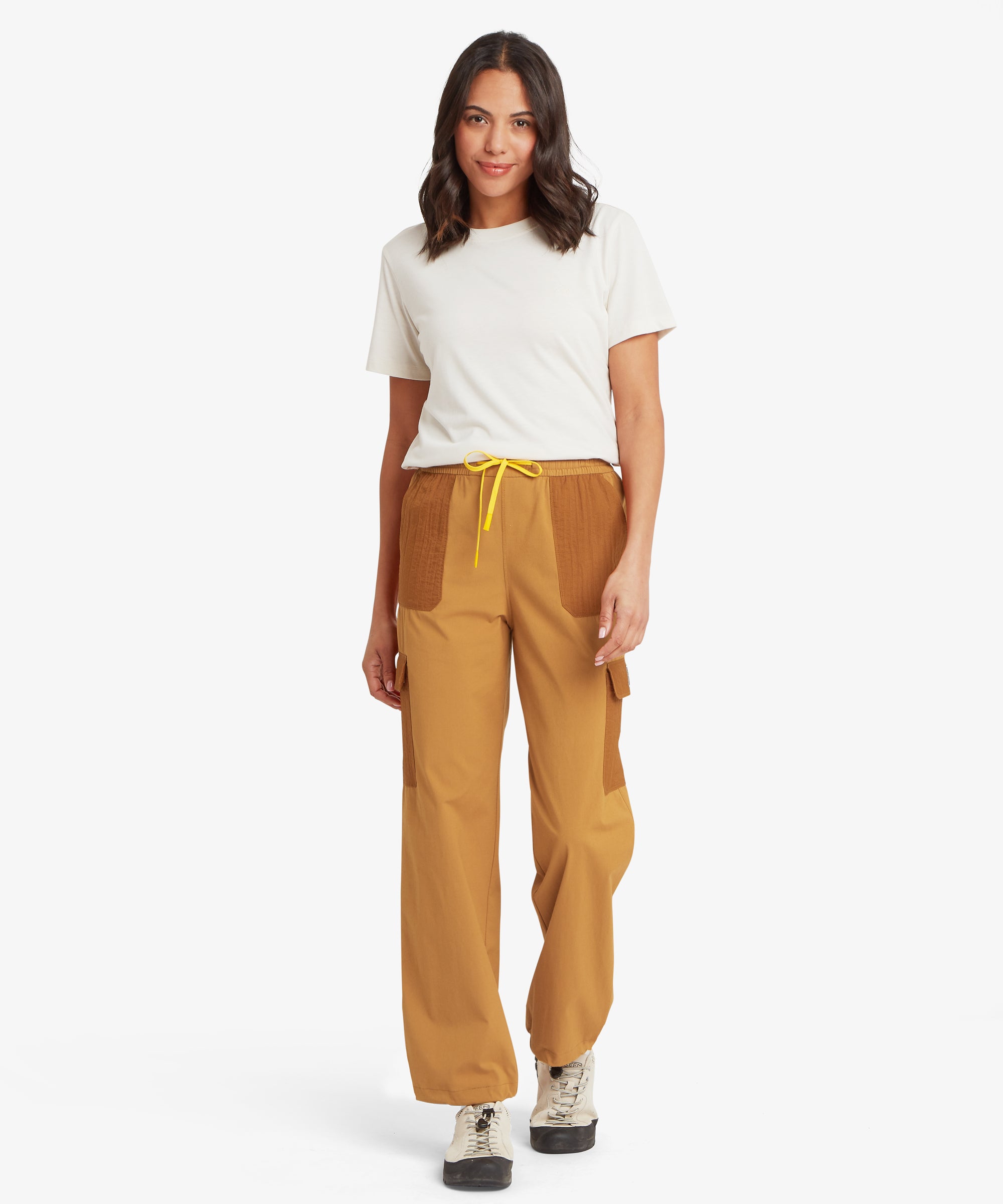 Woman wearing mustard-yellow utility trousers with a relaxed, straight-leg fit, elasticated waistband, and yellow drawcord, styled with a white T-shirt and trainers.