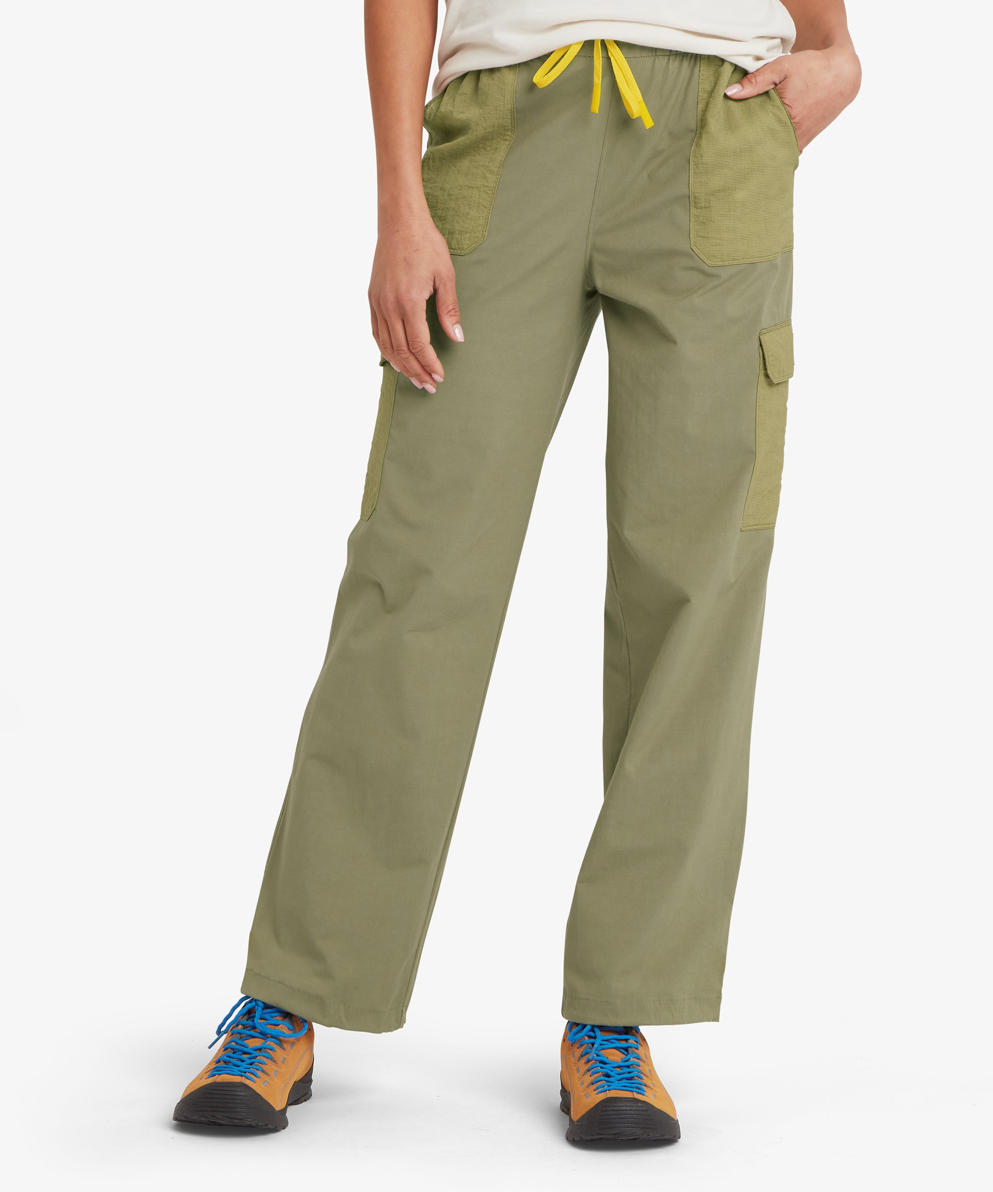 A person facing forward wearing a plain white short‑sleeve T‑shirt and olive cargo trousers with contrasting green pockets and a yellow drawstring. Tan hiking shoes with blue laces complete the outfit, shown against a plain white background.