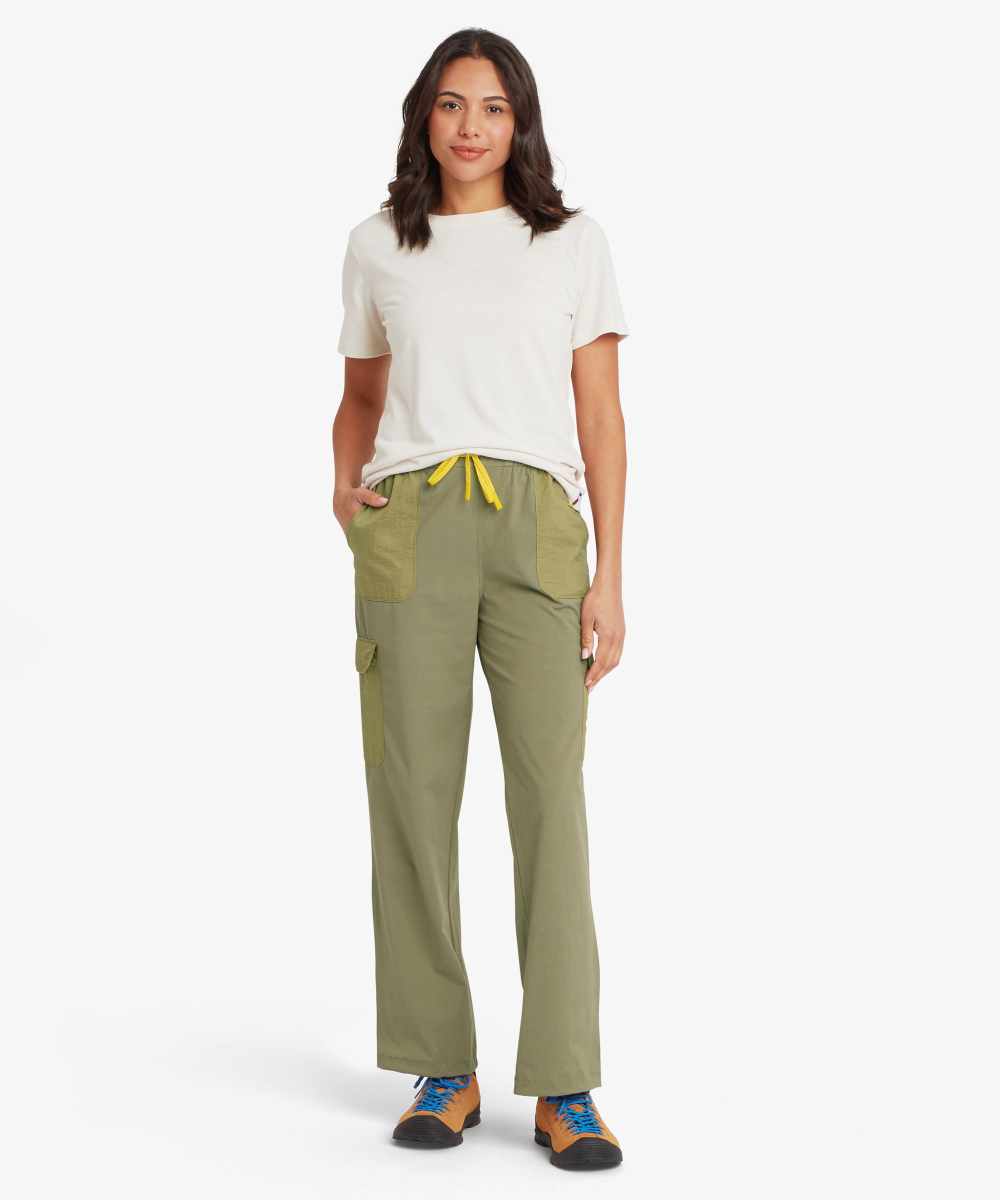 A person wearing olive cargo trousers with a yellow drawstring and multiple pockets, paired with tan hiking shoes with blue laces. The relaxed fit and functional design are shown clearly against a plain white background.