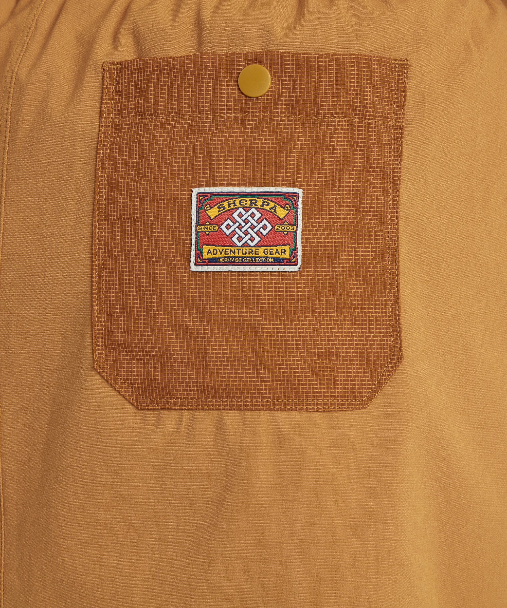 Close-up of mustard-yellow skort showing a textured pocket with a Sherpa Adventure Gear patch and snap button closure.
