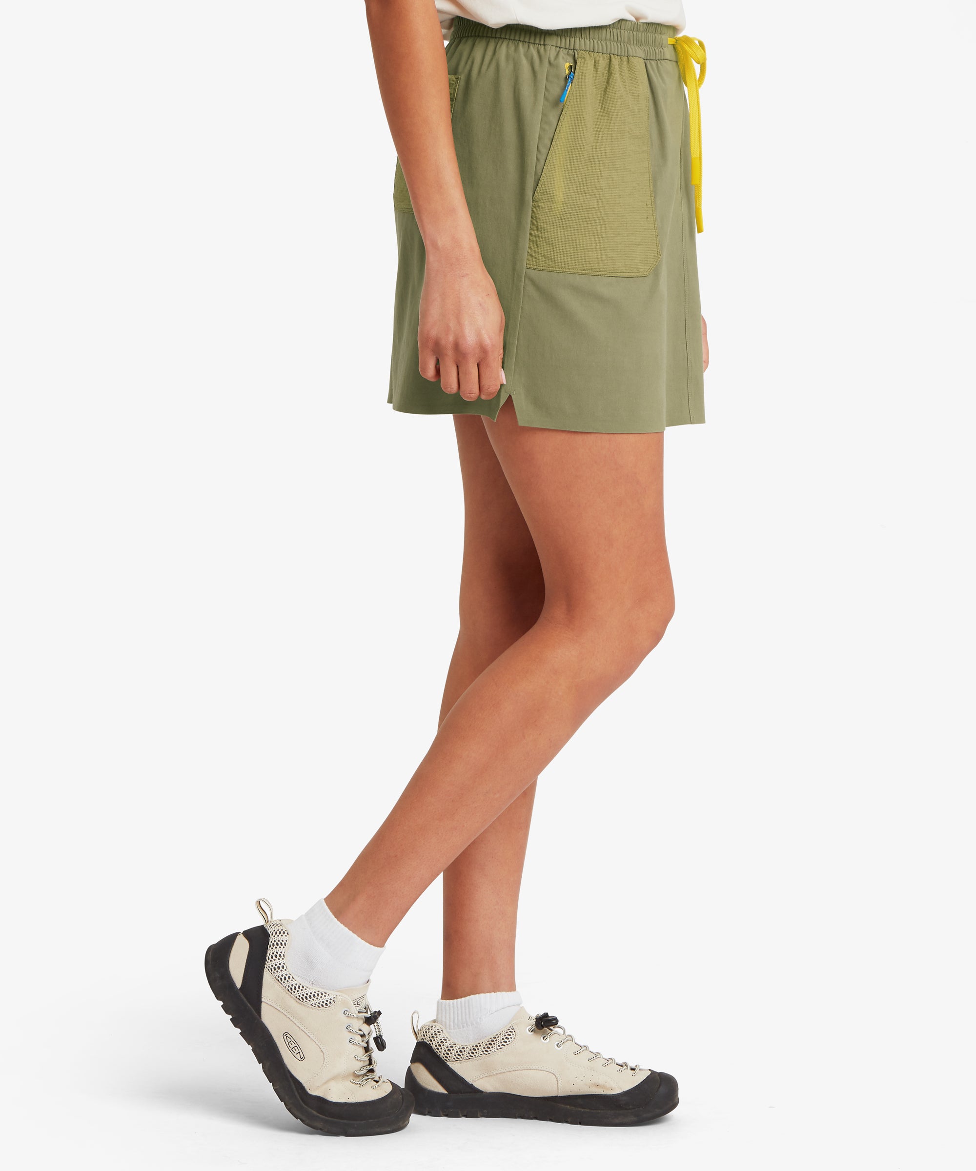 Side view of a female model wearing an olive green skort with a comfortable, easy fit through the hips and a straight hemline that falls above the knee.