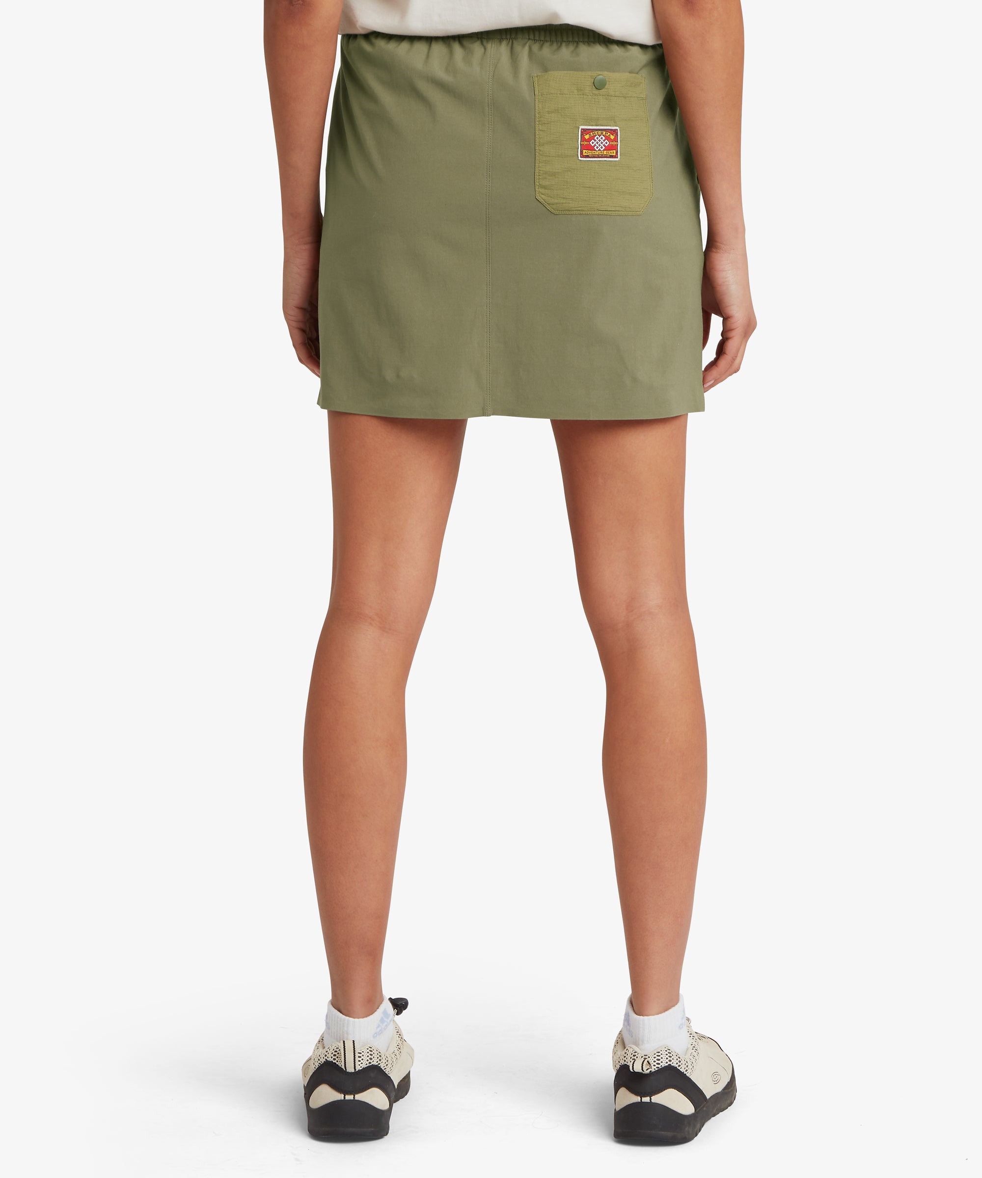 Back view of a female model wearing an olive green skort with a relaxed fit and elastic waistband, showing smooth coverage through the seat and upper thighs.
