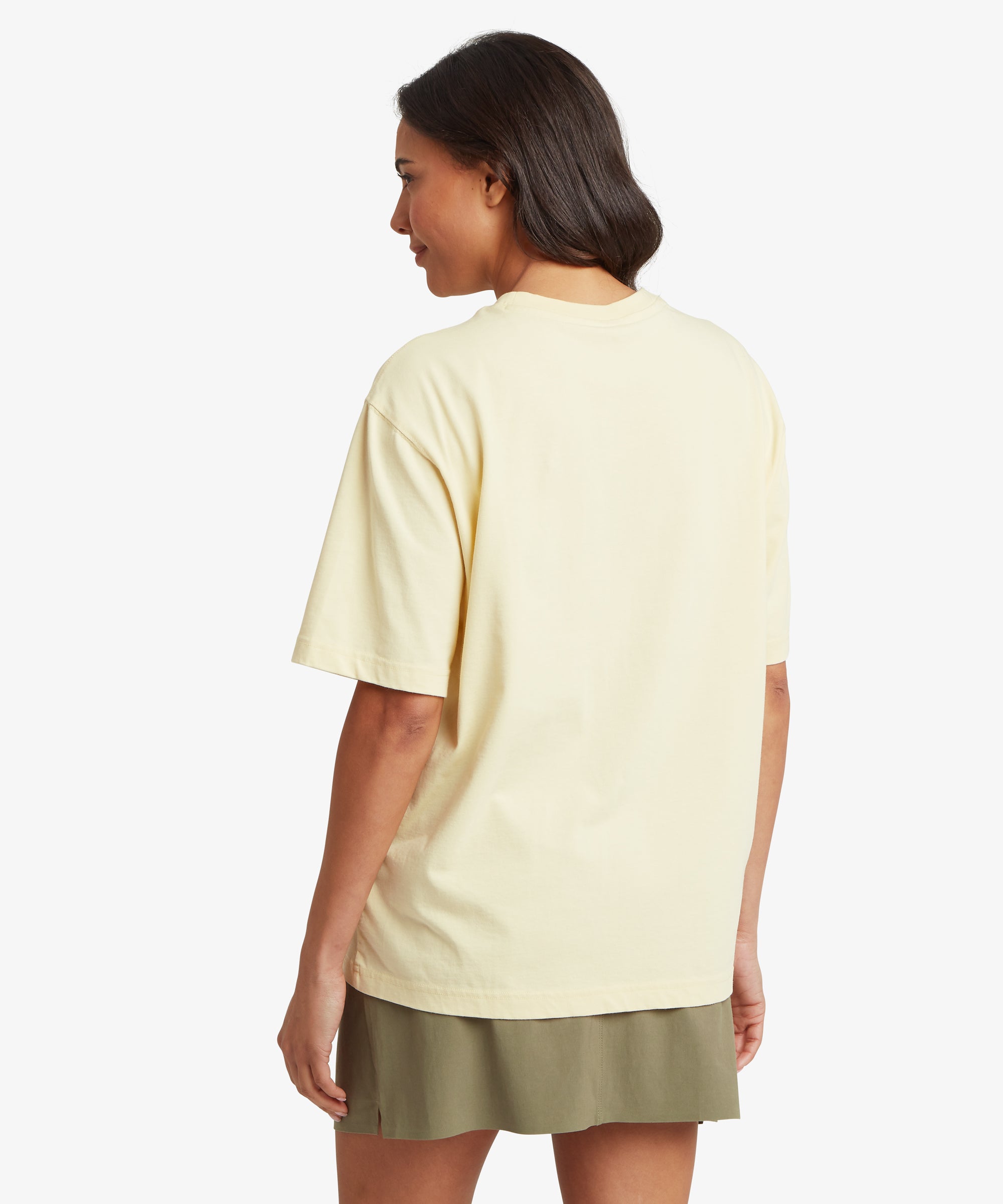 RŸckansicht einer Frau, die ein cremefarbenes Kurzarm-T-Shirt mit lockerer Passform und schlichtem, unbedrucktem RŸcken trŠgt, das leicht unterhalb der HŸften endet.