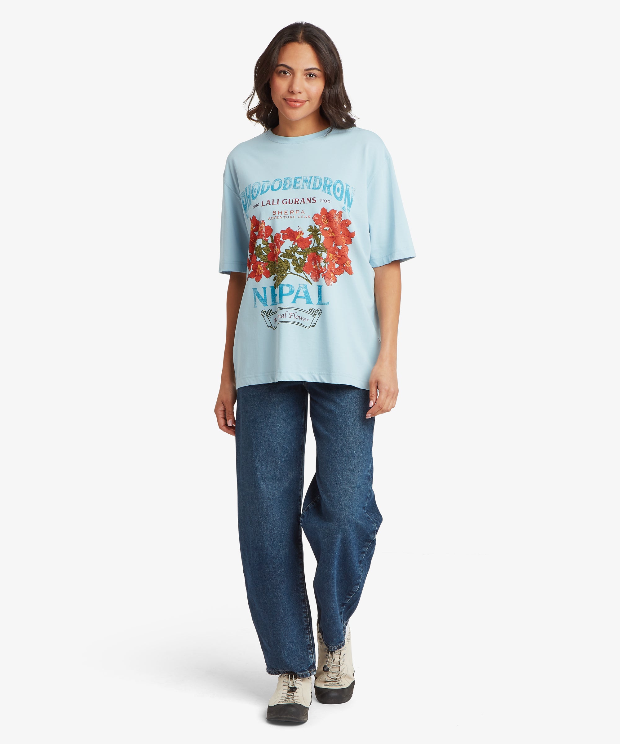 Frau, die vorwŠrts geht und ein hellblaues T-Shirt mit Grafikprint trŠgt, das durchgehend und an den €rmeln locker und oversized geschnitten ist, dazu eine gerade geschnittene blaue Jeans und lŠssige Sneakers.