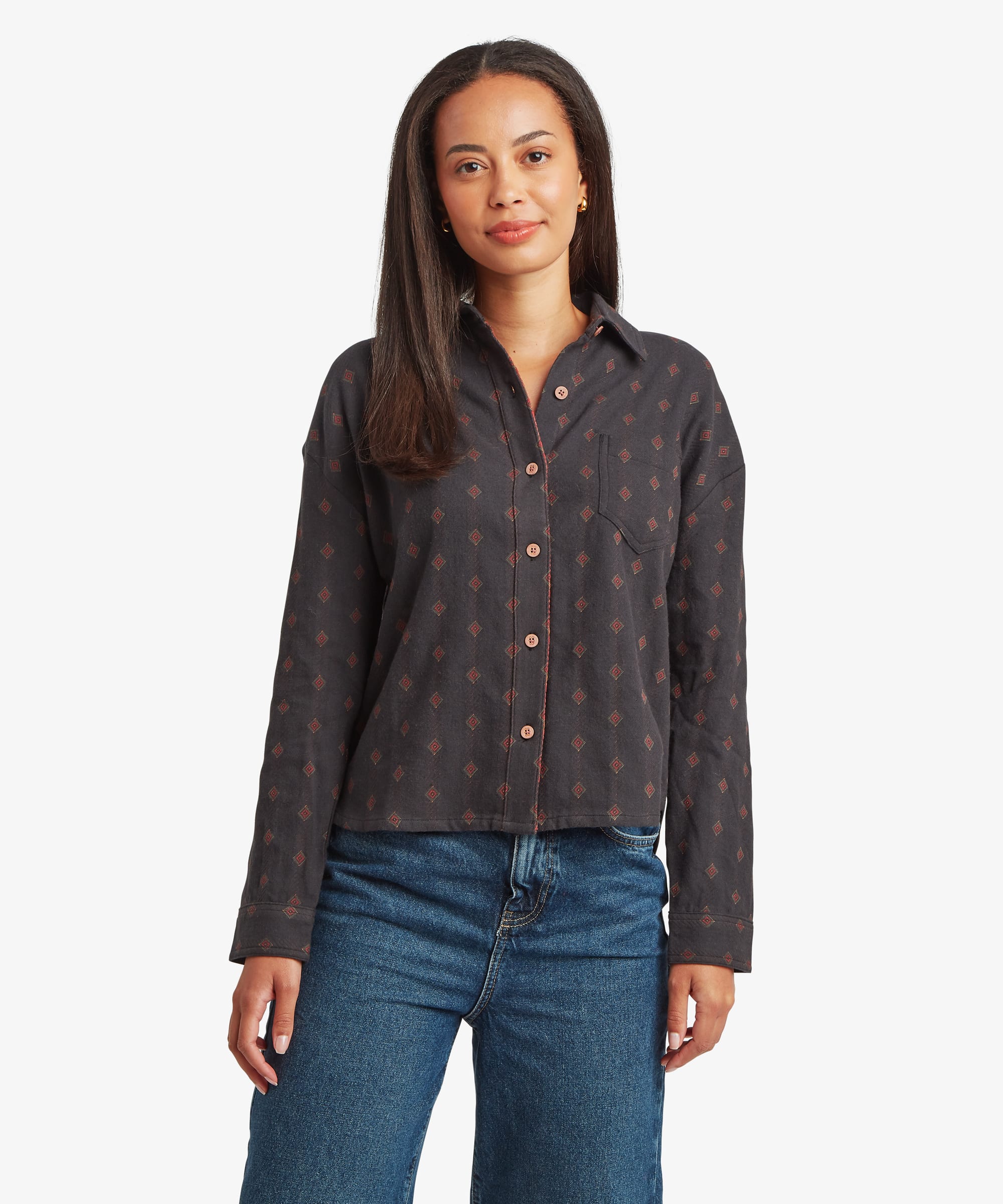 Woman wearing a black long-sleeve button-up shirt featuring an allover geometric print in warm earth tones. Designed with a pointed collar, button-front closure, and a relaxed fit.