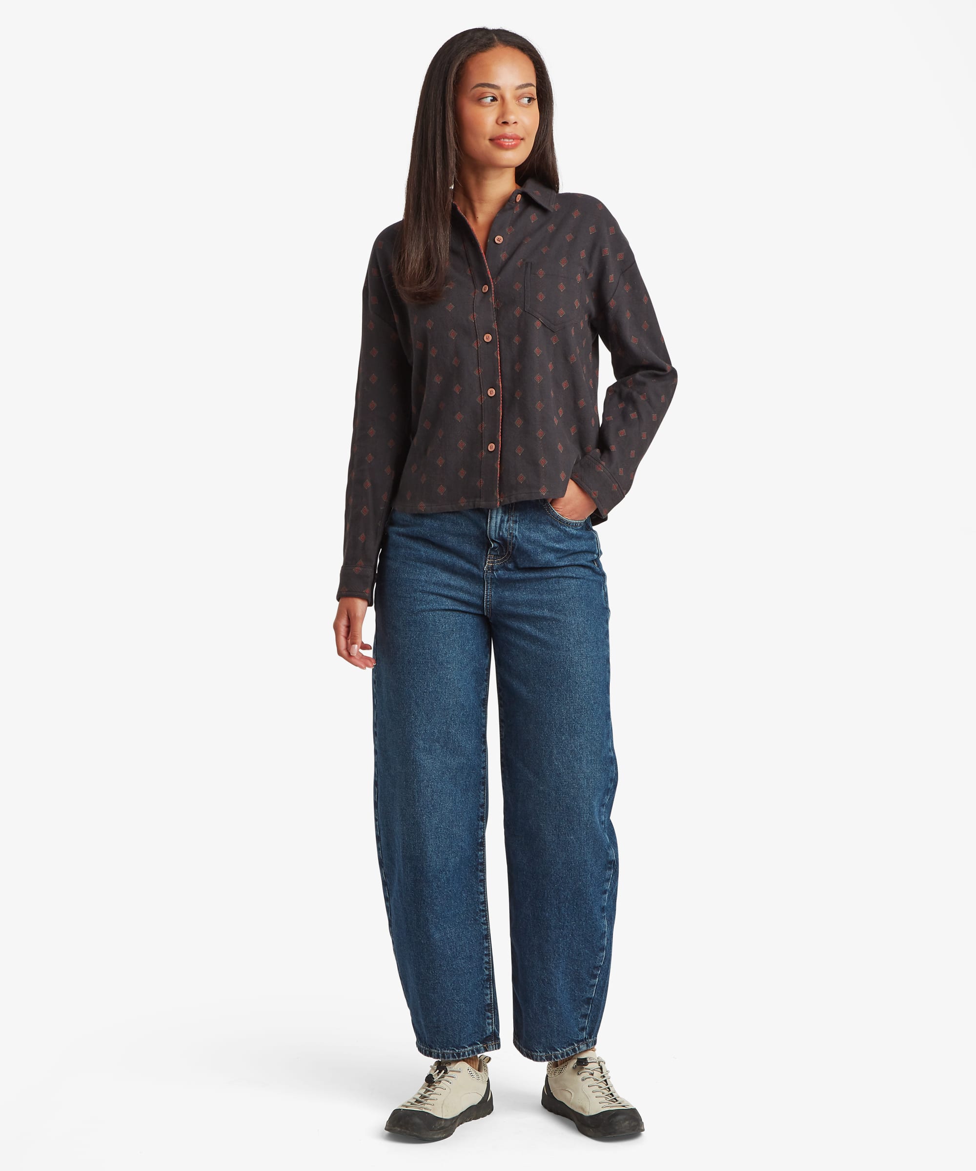 Full-body front view of a woman wearing a black long-sleeve button-up shirt with an allover geometric print. Styled with blue jeans to showcase the relaxed silhouette and curved hem.