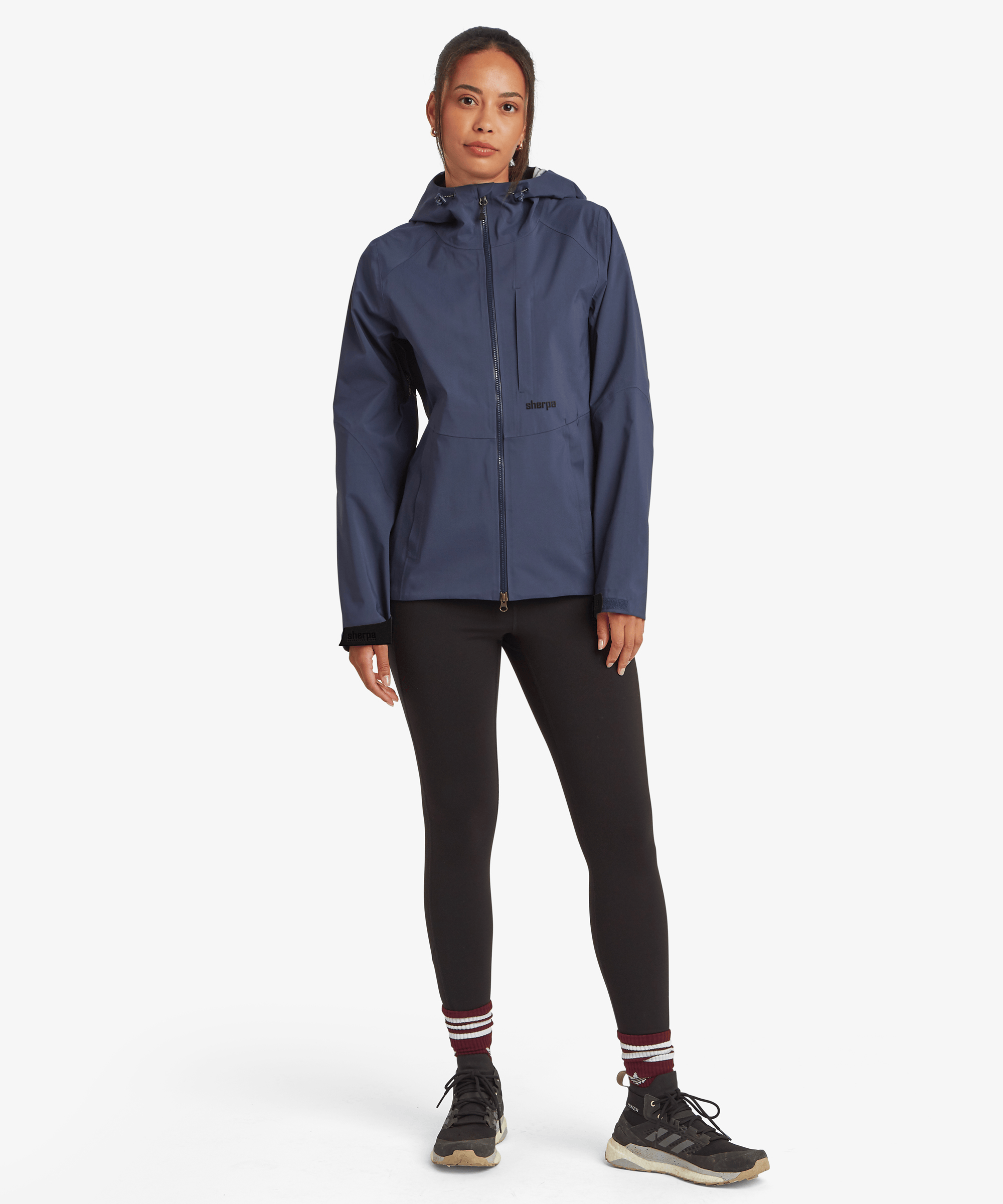 Full-body front view of the Women's Beyul 3-layer jacket in blue, paired with black leggings and hiking shoes.