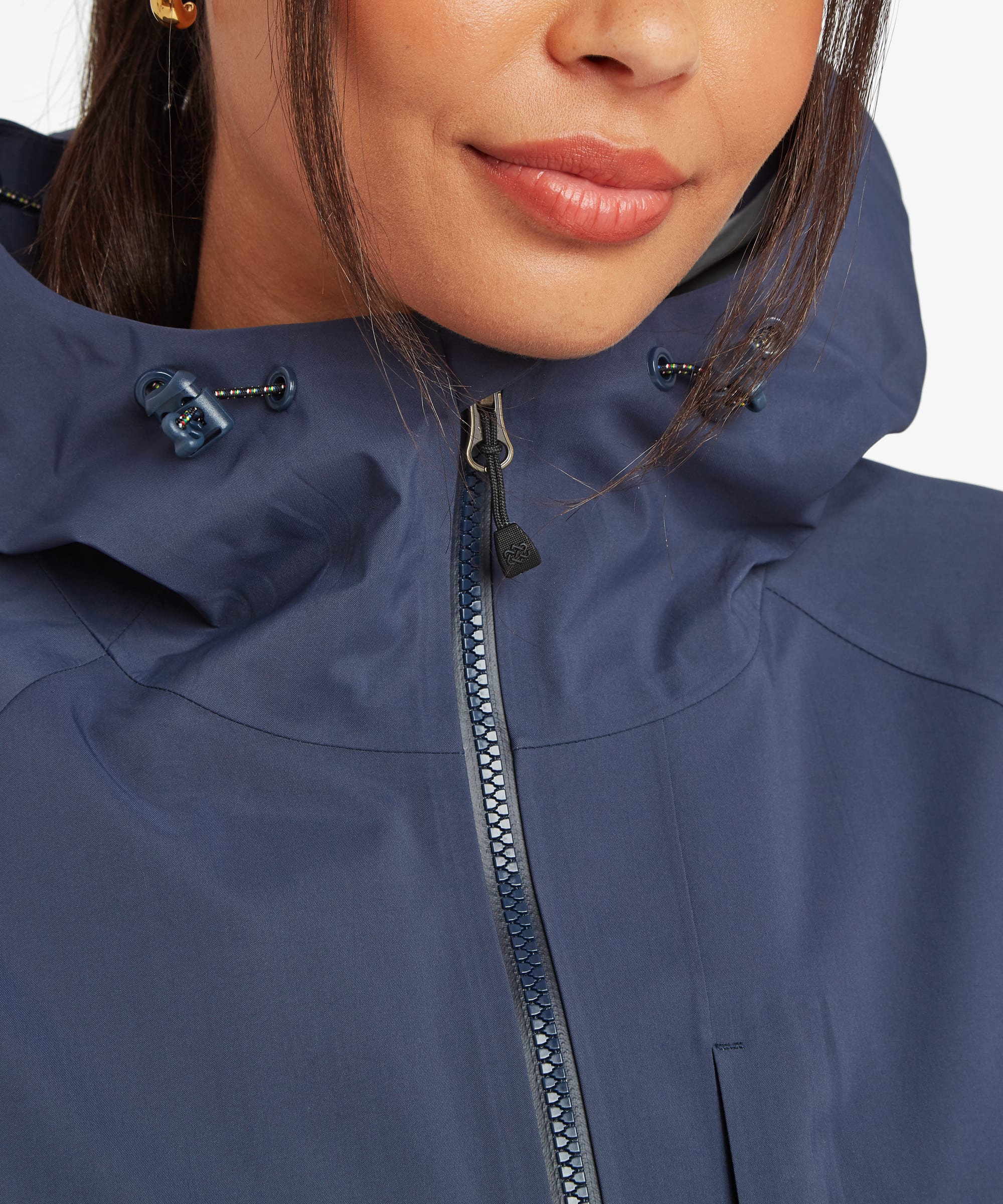 Close-up of a woman wearing a blue waterproof shell jacket featuring a waterproof front zipper, adjustable hood, and technical outerwear detailing.