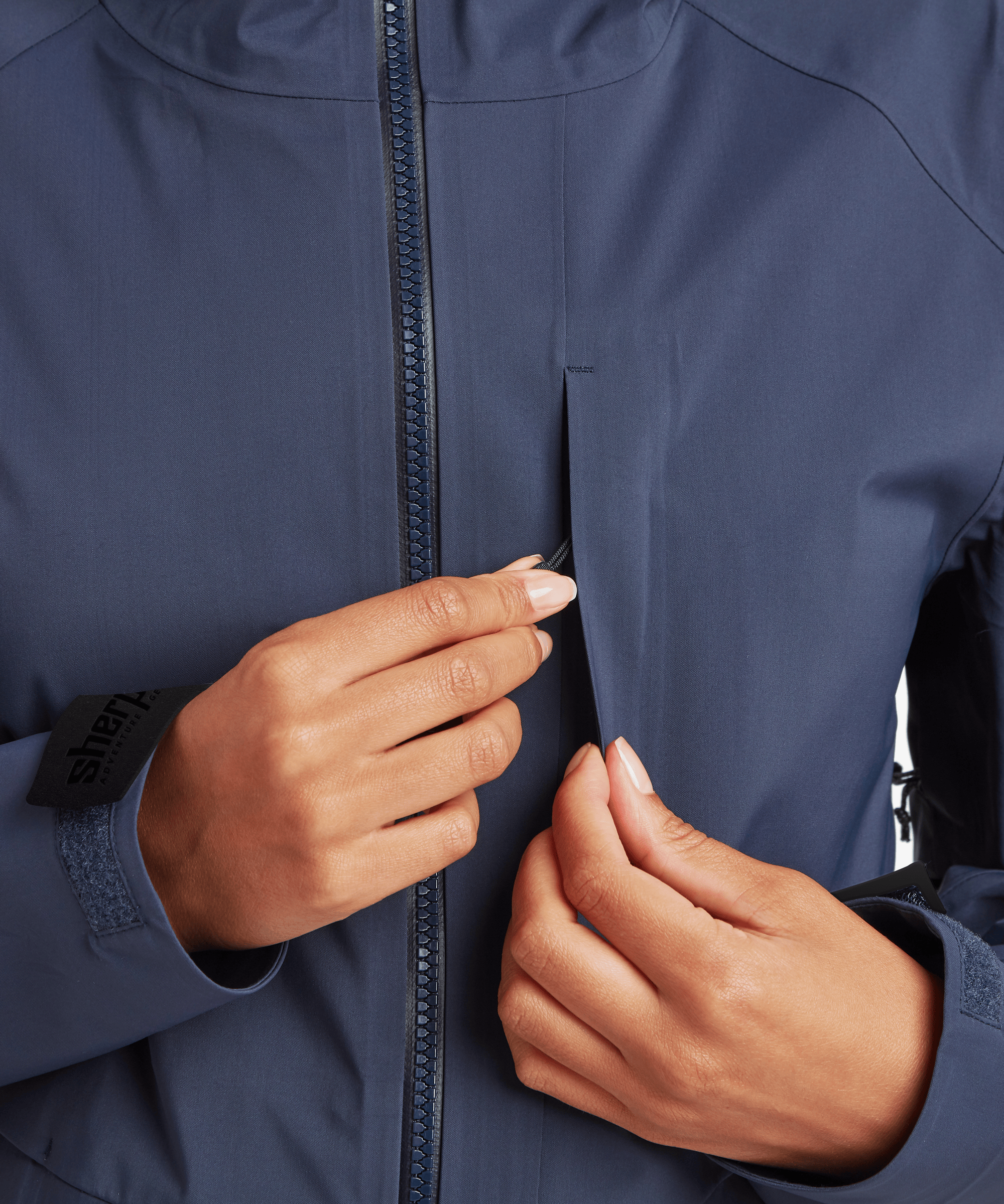 Detail view of the Women's Beyul 3-layer jacket in blue showing the front waterproof zipper and storm flap construction.