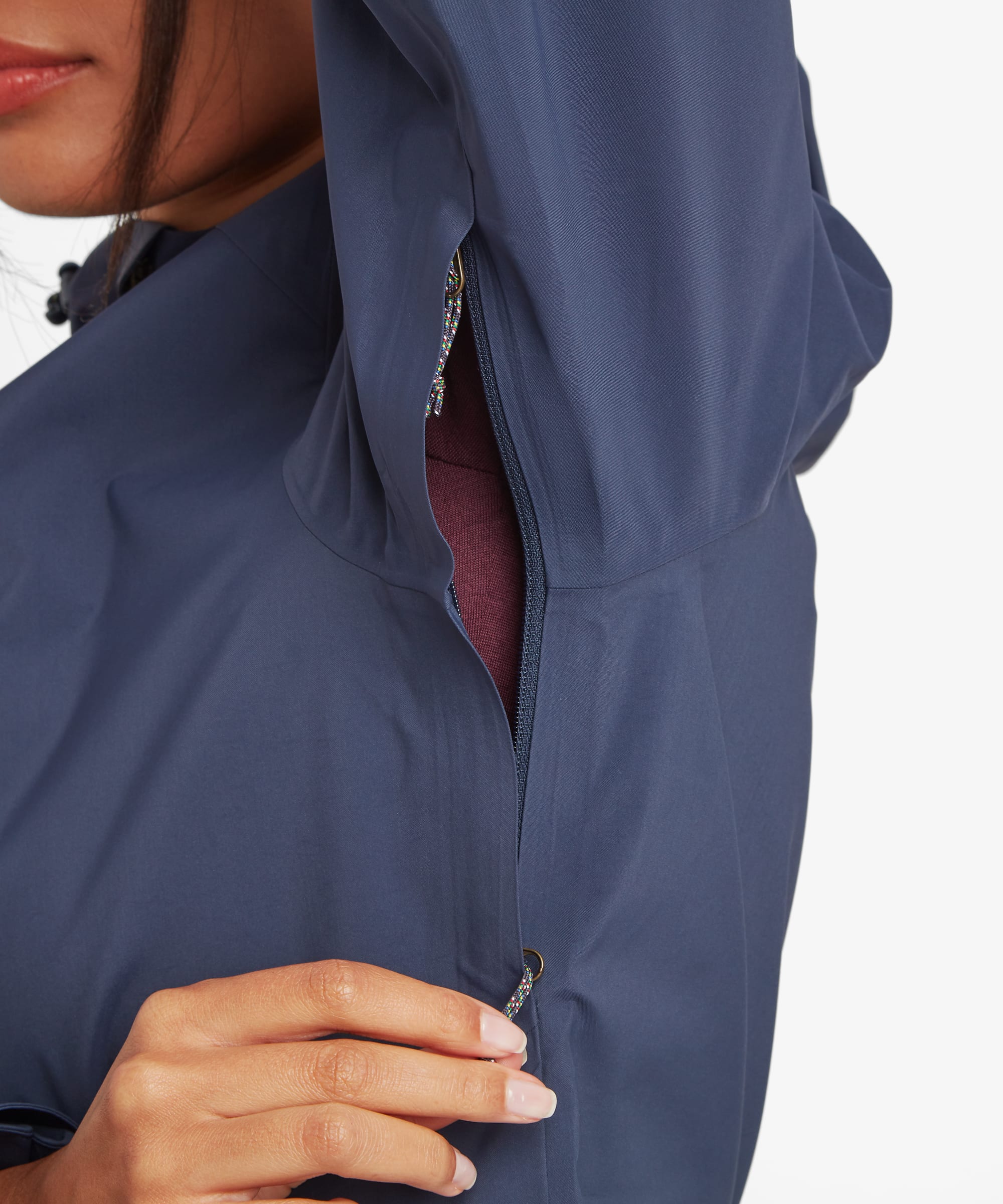 Close-up of a woman wearing a blue waterproof shell jacket showing an underarm ventilation zipper designed for breathability and temperature regulation.