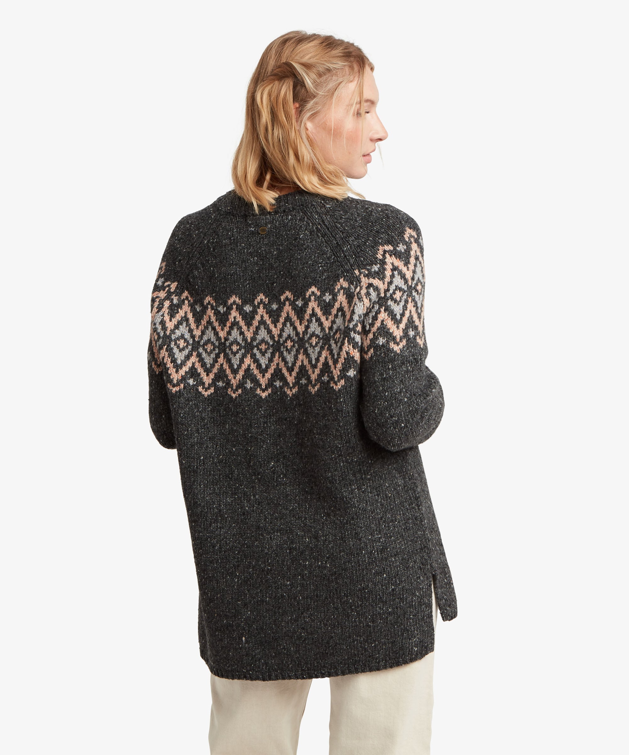 A female model, shown from a rear three-quarter angle, wearing the Sherpa Adventure Gear Dumji Long Sweater in black. The longer knitted sweater extends over the hips and features long sleeves and a ribbed neckline, while the cream and beige geometric pattern continues around the upper back and sleeves.