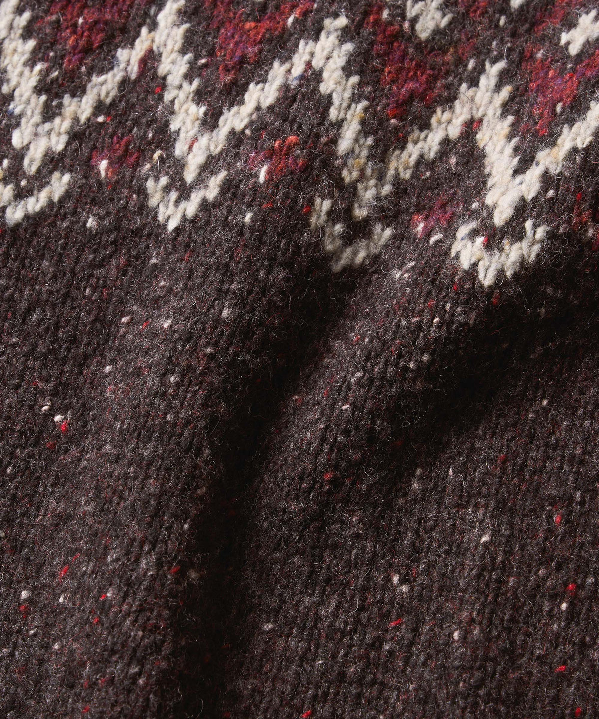 Close-up of a dark brown heathered knit fabric with a cream and red zigzag pattern near the top.