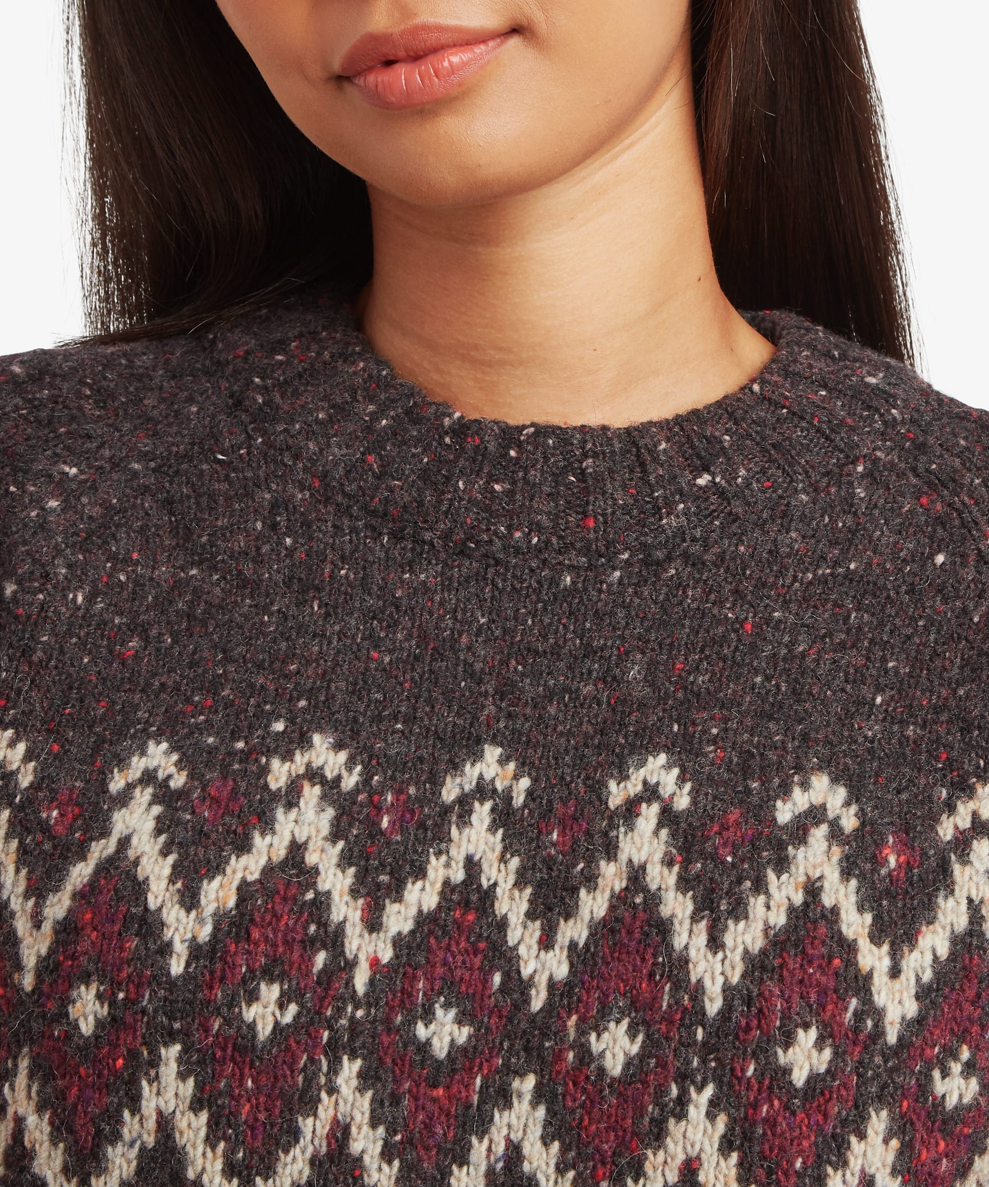 Close-up detail of a woman wearing a charcoal-black Fair Isle sweater. The image highlights the textured knit fabric and intricate burgundy, cream, and grey geometric pattern across the chest.