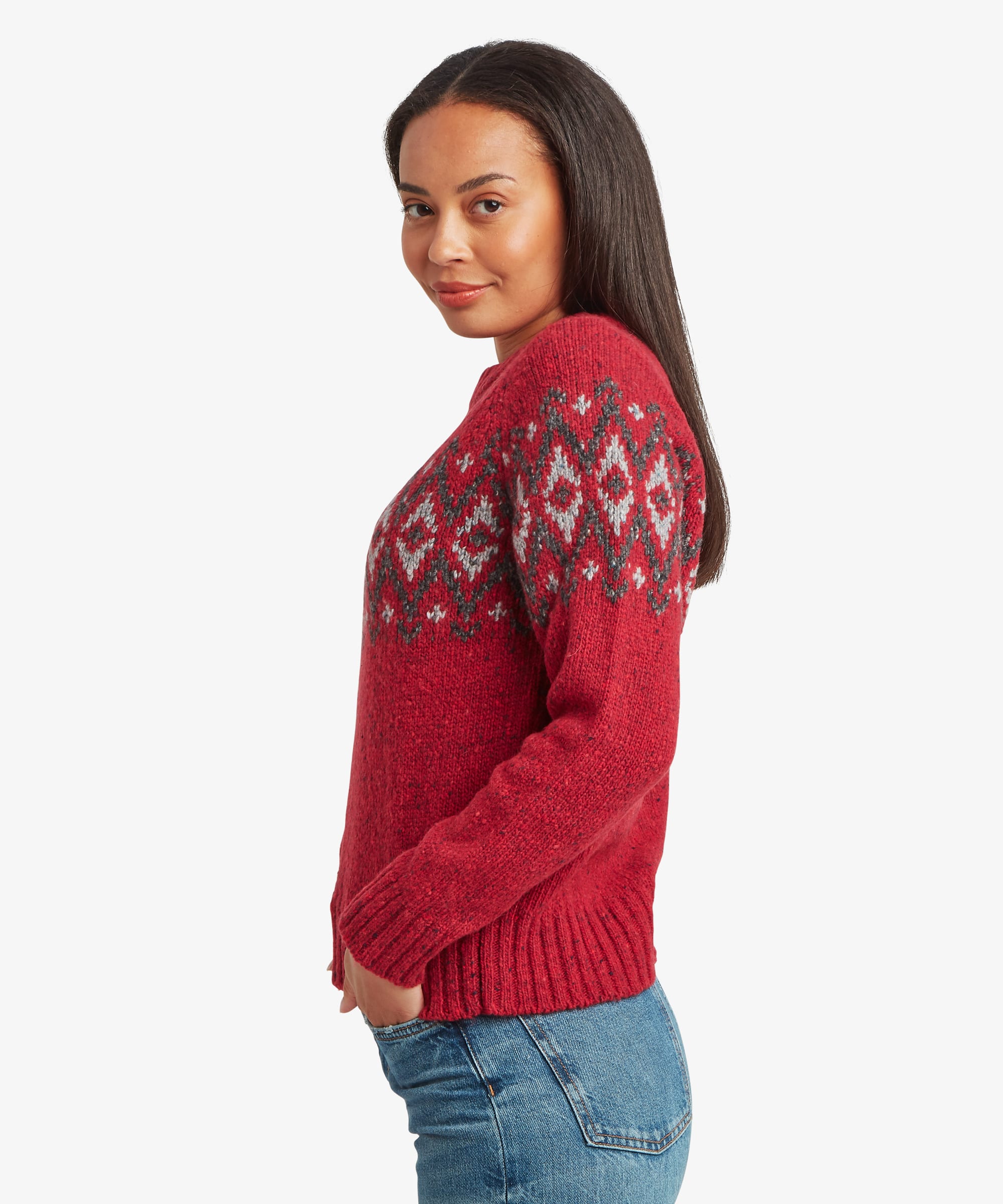 Side profile of a woman wearing a red patterned knit sweater. The image highlights the relaxed fit, ribbed cuffs, and wraparound Fair Isle design.